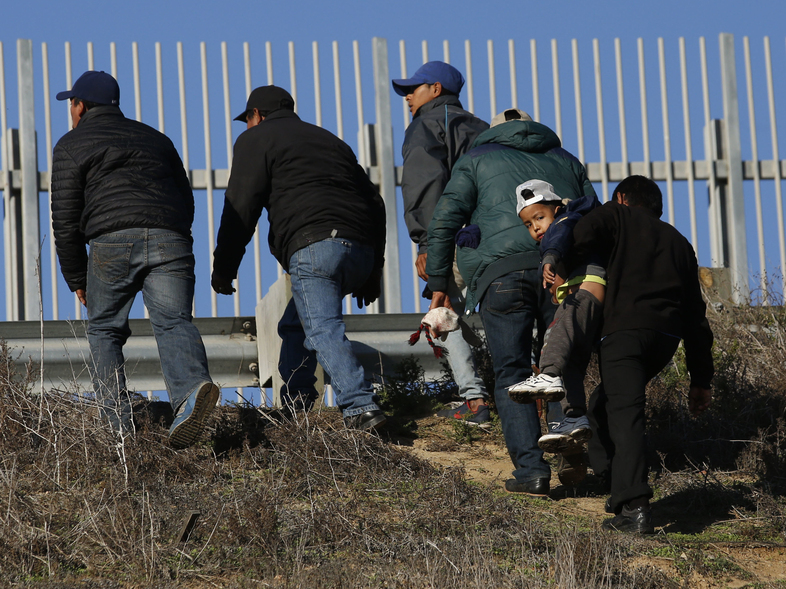 Migrants, one carrying a child, who plan to turn themselves over to U.S. border agents, walk up the embankment after climbing over a U.S. border wall from Playas de Tijuana, Mexico, last week. On Tuesday, members of the Hispanic Caucus called for improved medical facilities and trained personnel at ports of entry. (Moises Castillo/AP)