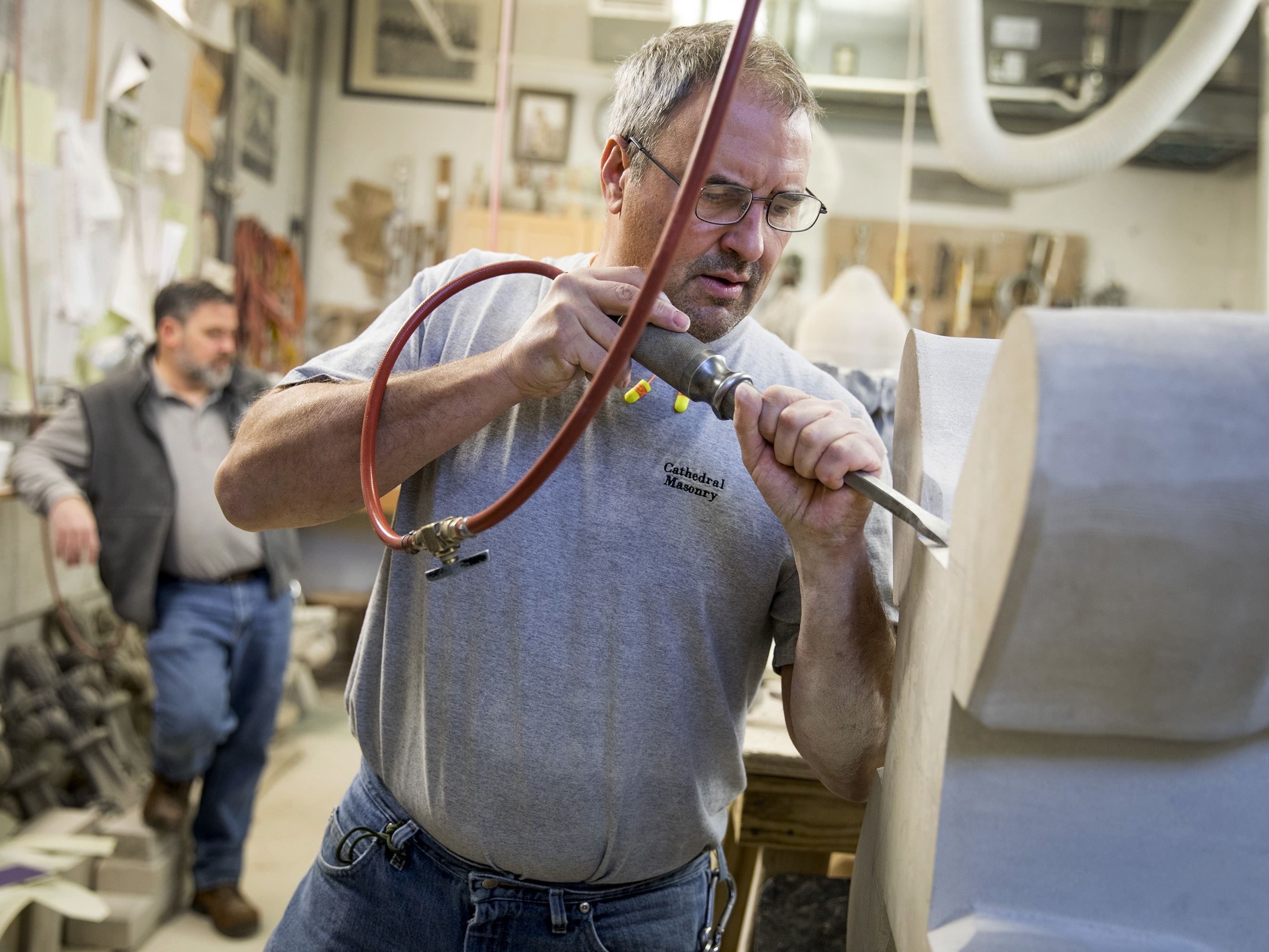Chip By Chip, Restoring The Damaged Washington National Cathedral 3 Stonemason Andy Uhl carves the base of a replacement finial that was damaged during the 2011 earthquake with Sean Callahan, fellow National Cathedral stonemason, stands behind him.
