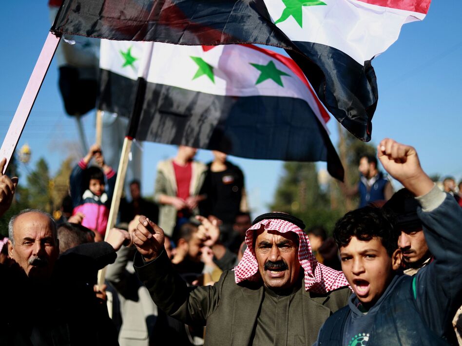 Syrian demonstrators wave the national flag during a demonstration in the Kurdish-majority city of Qamishli in northeastern Syria on Sunday, asking for the Syrian army's protection as Turkey threatens to carry out a fresh offensive following the U.S. decision to withdraw troops. (Delil Souleiman/AFP/Getty Images)