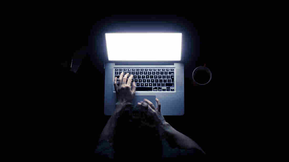 Woman using a laptop computer in darkness with her hands illuminated by the computer screen isolated on black background