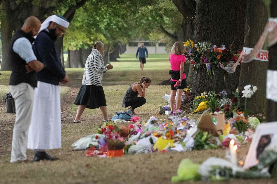 People on Tuesday stand next to floral tributes placed across the road from the Al Noor Mosque in Christchurch, New Zealand, where dozens of worshippers were gunned down last week. (Marty Melville/AFP/Getty Images)