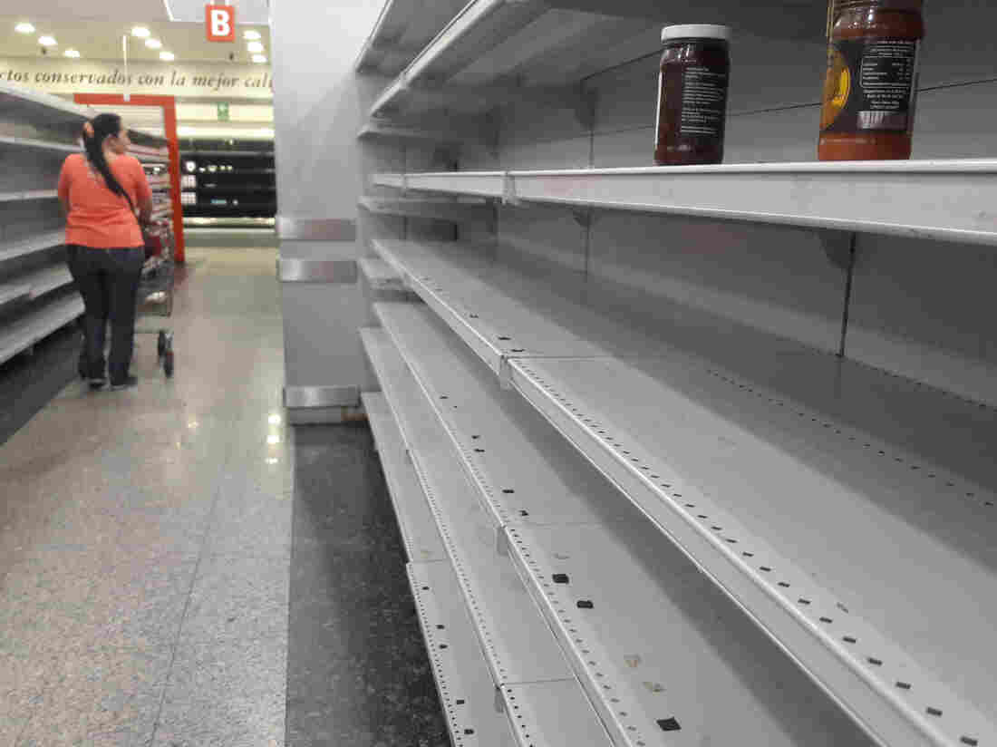 A woman walks between the empty shelves of a supermarket in Caracas on January 11, 2018.
