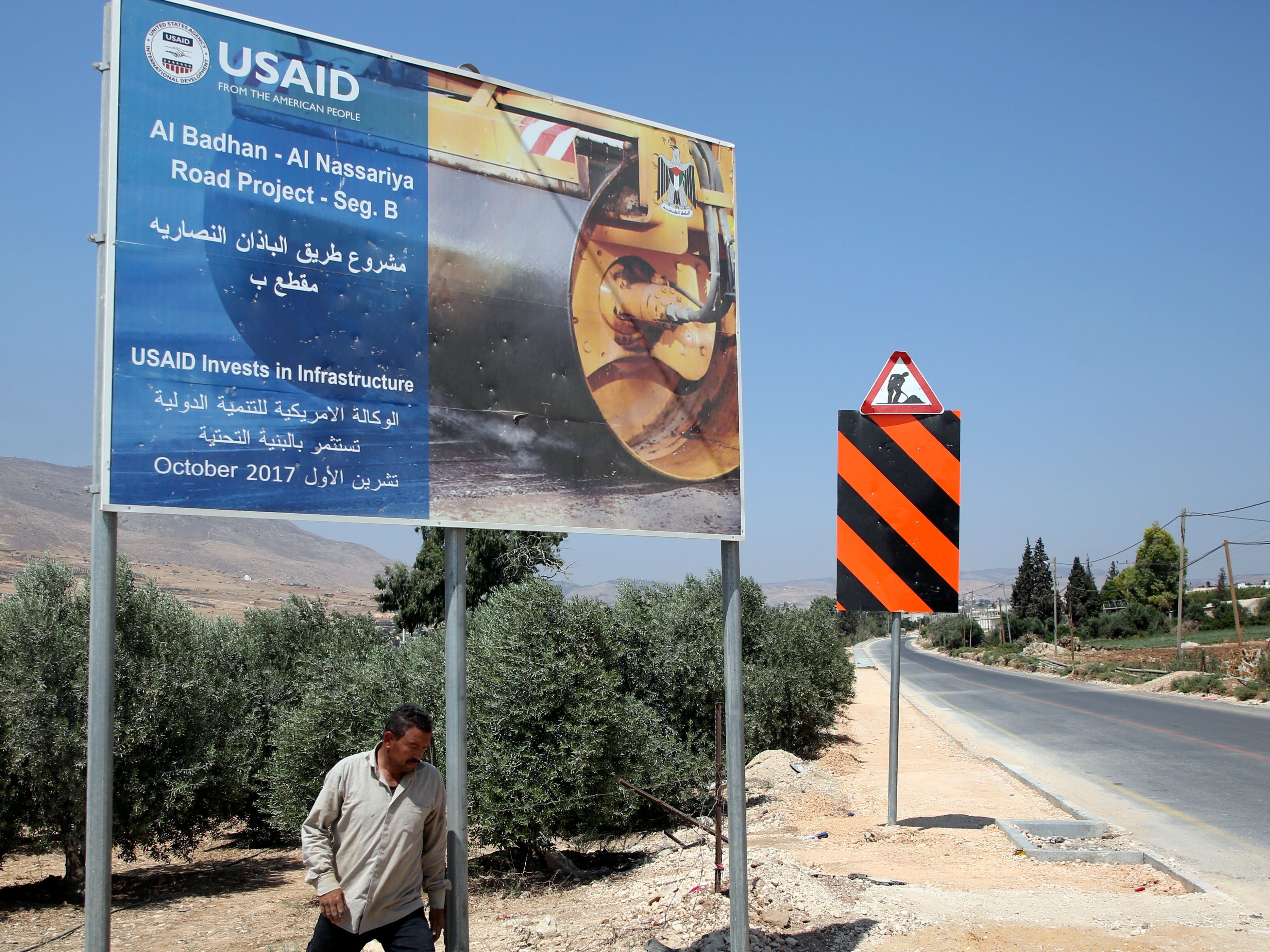 A Palestinian man walks near a USAID billboard in the West Bank village of Badhan, north of Nablus, last August. Since January, U.S. financing for humanitarian programs serving Palestinians has been suspended (AFP/Getty Images)