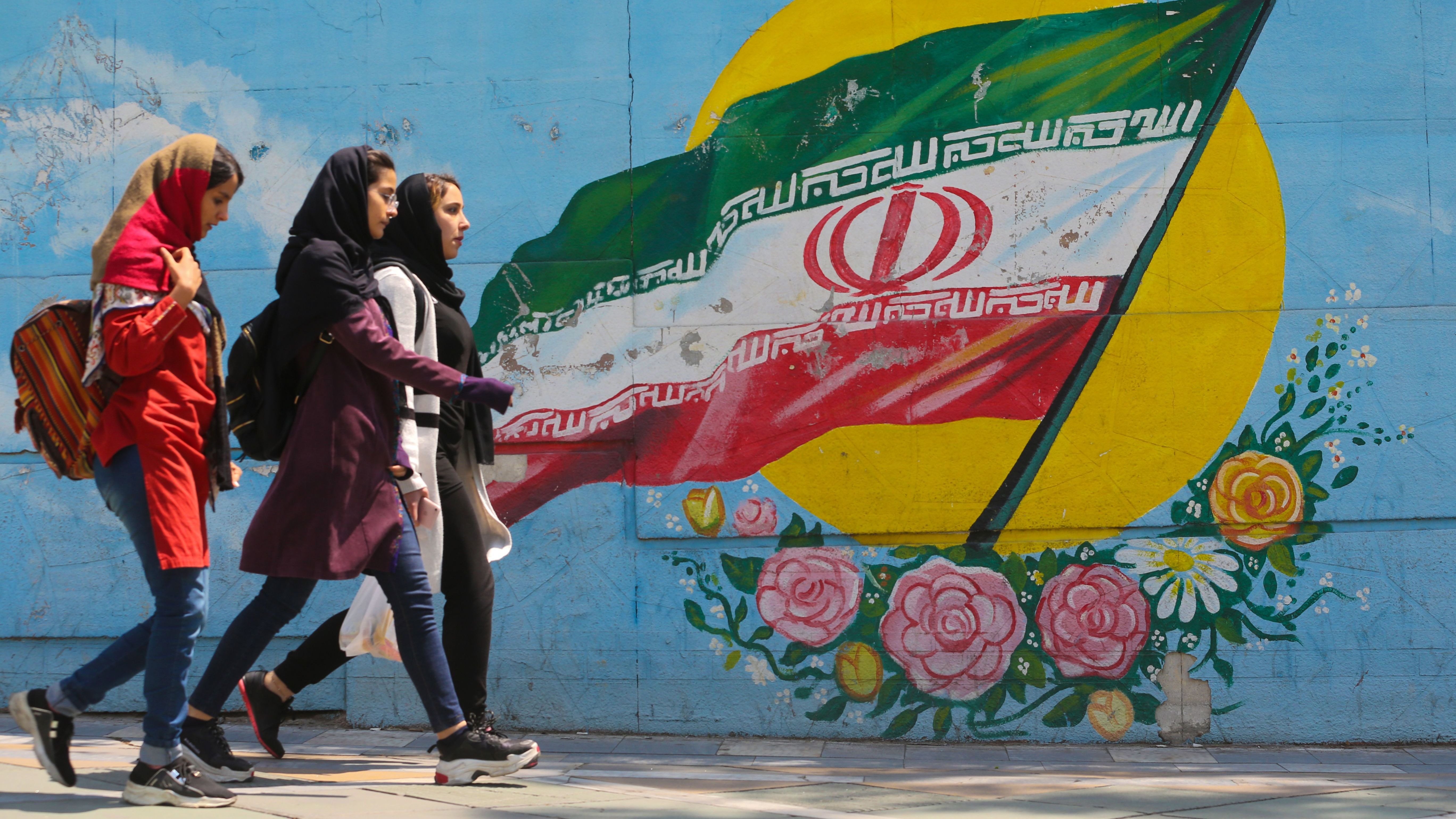 Young women walk past a mural showing the Iranian flag in Tehran on April 23. The White House announced Monday it was ending waivers exempting several countries from U.S. sanctions on Iranian oil exports.