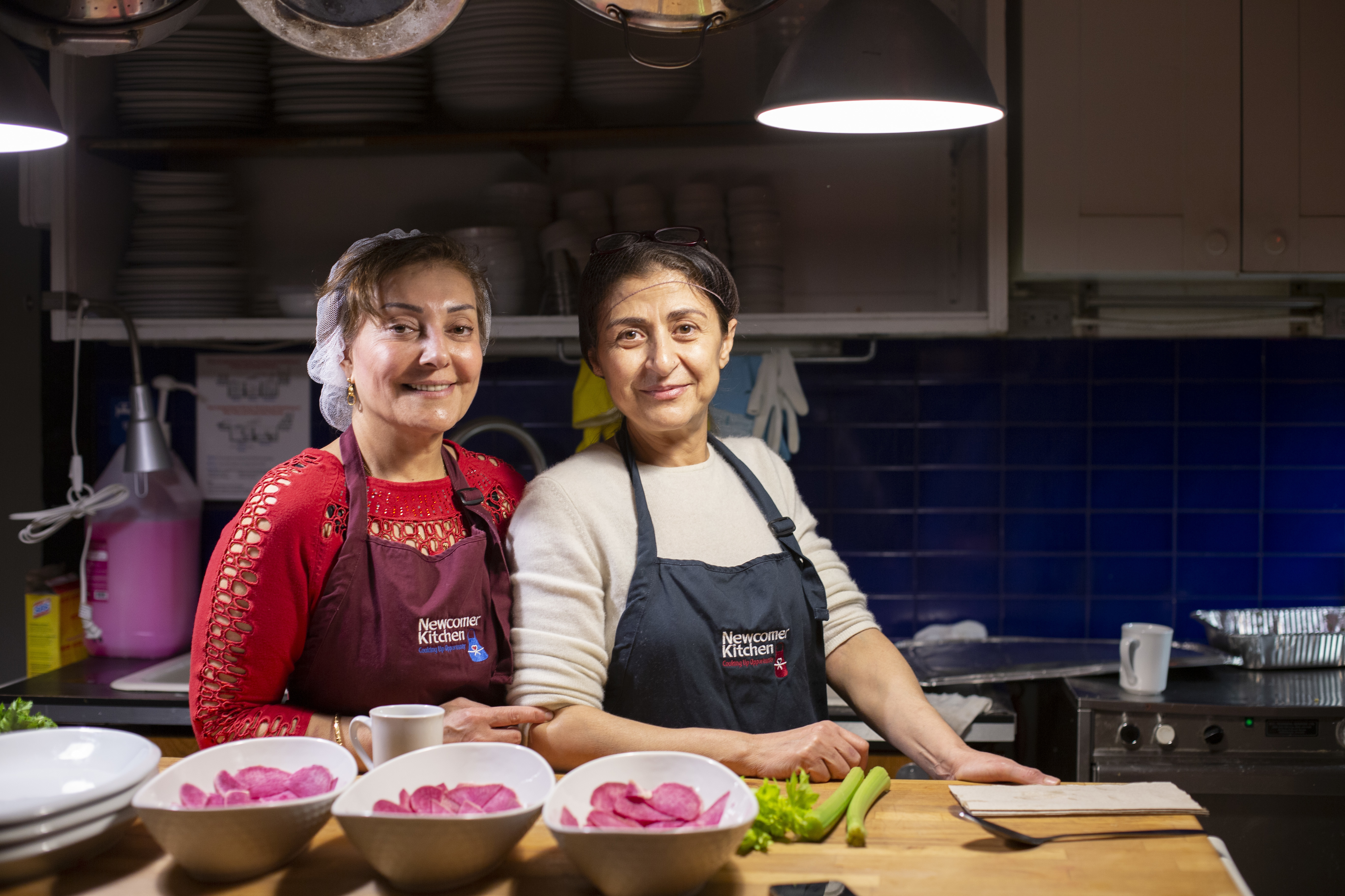 Two Syrian refugees, Narwal Alakayleh (left) and Lina AlAlssantin (right), prepare for a pop-up dinner of Levantine food at Newcomer Kitchen.