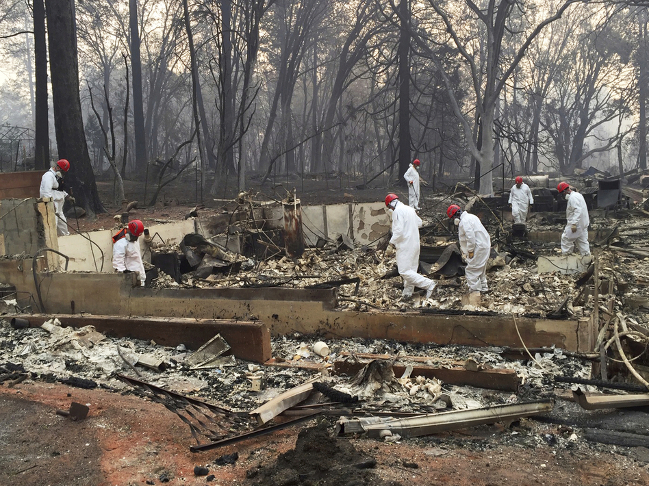 Volunteer rescue workers search for human remains in the rubble of homes burned in the Camp Fire in Paradise, Calif. State officials say the fire was caused by PG&E power lines.