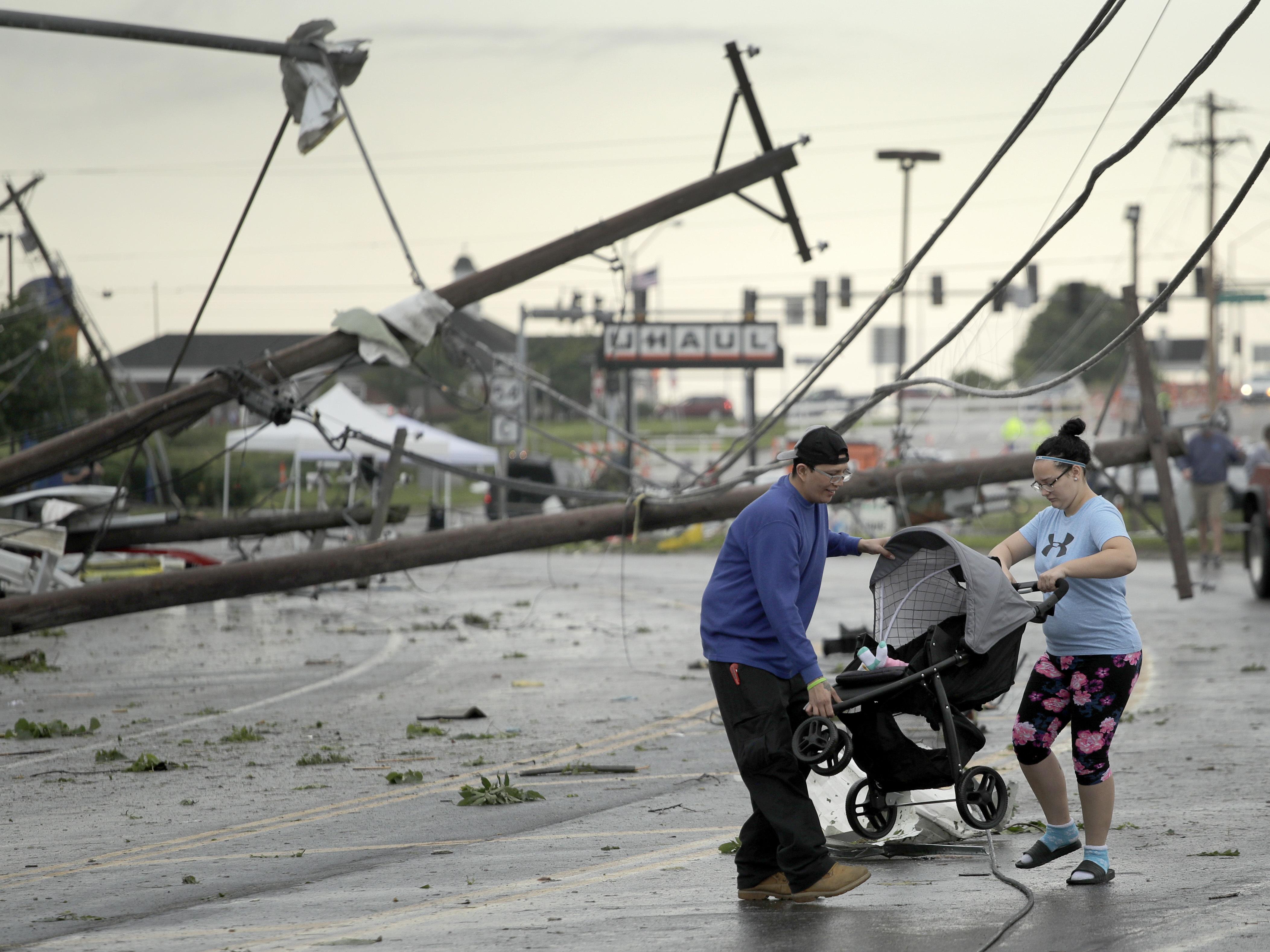 Jessica Rodgers and neighbor Ray Arellana carry a stroller carrying Rodgers' sister Sophia Rodgers over downed power lines as they head to Rodgers' mother's apartment to check on damage on Thursday after a tornado tore though Jefferson City, Mo., late Wednesday.