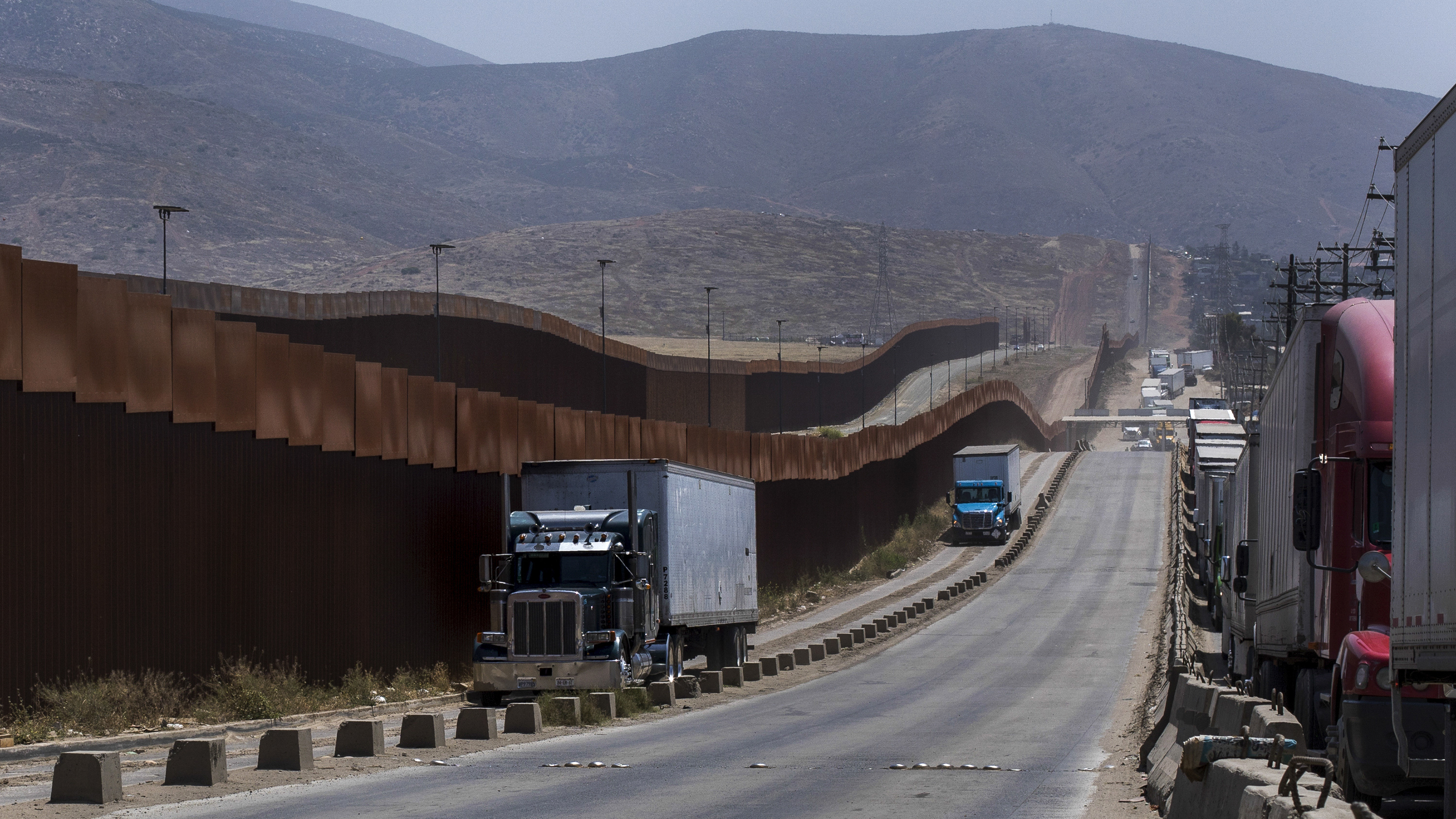 Trucks pass along a border wall as they get into position to cross into the United States at the border in Tijuana, Mexico, on Friday. Companies have been rushing to ship as many goods as possible out of Mexico to get ahead of possible tariffs threatened by President Donald Trump, hurriedly sending cars, appliances and construction materials across the border to beat Monday