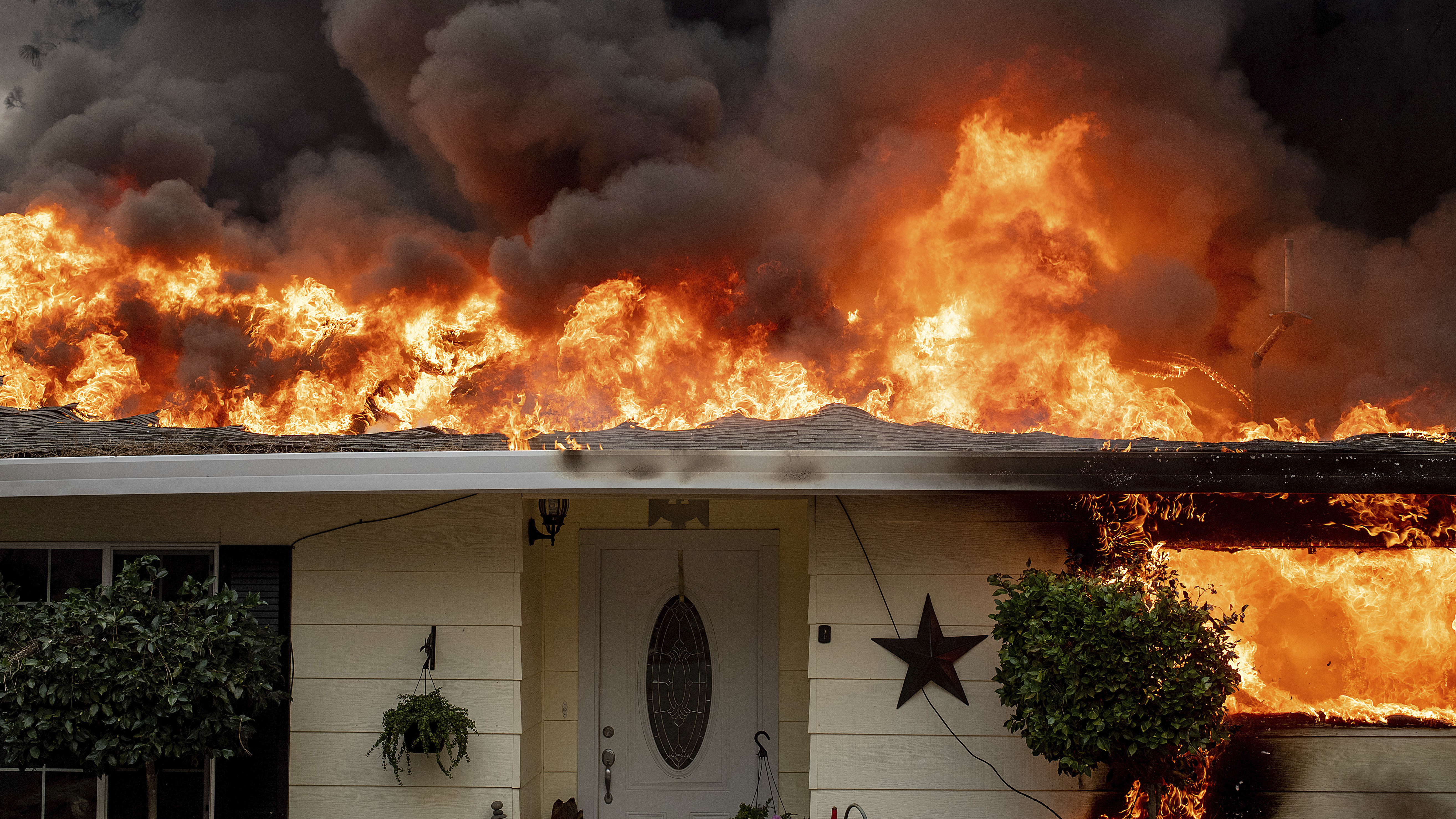 Flames consume a home in Paradise, Calif.  PG&E will pay the town and other jurisdictions $1 billion for wildfire damages caused by its equipment.