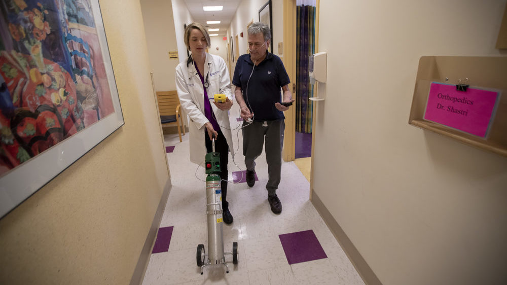 Dr. Mary Rice walks with Michael Howard at a Beth Israel Deaconess HealthCare clinic in Chealsea, Mass, as they test his oxygen levels with the addition of oxygen from a portable tank. He has COPD, a progressive lung disease that can be exacerbated by heat and humidity.