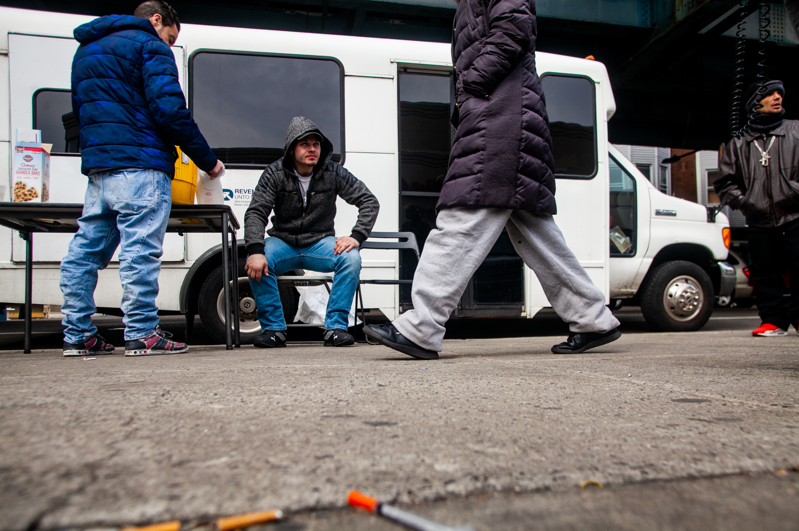 A bus run by the organization Prevention Point parks at Kensington and Allegheny avenues in Philadelphia to offer harm-reduction services to drug users in the area. Louis Morano (center), who was visiting the Prevention Point bus for the second time, sits outside and waits to be seen by Dr. Ben Cocchiaro. (Brad Larrison for WHYY)