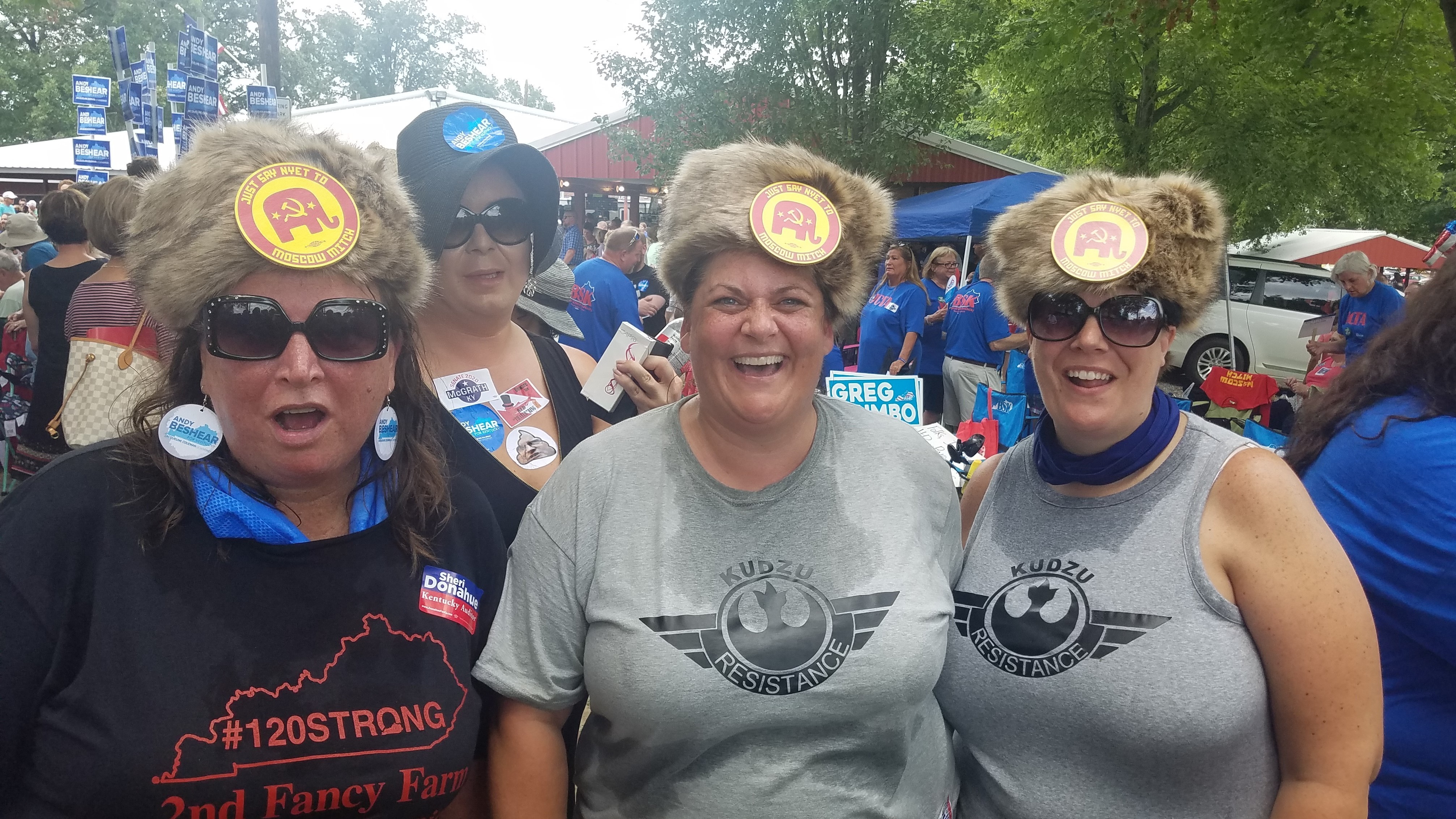 The August heat at a political event did not deter (from left) Laura Hartke, Christina Trosper and Katie Hancock from wearing their Russian-styled fur hat with buttons saying: &quot;Say Nyet To Moscow Mitch.&quot; (Kentucky Public Radio)