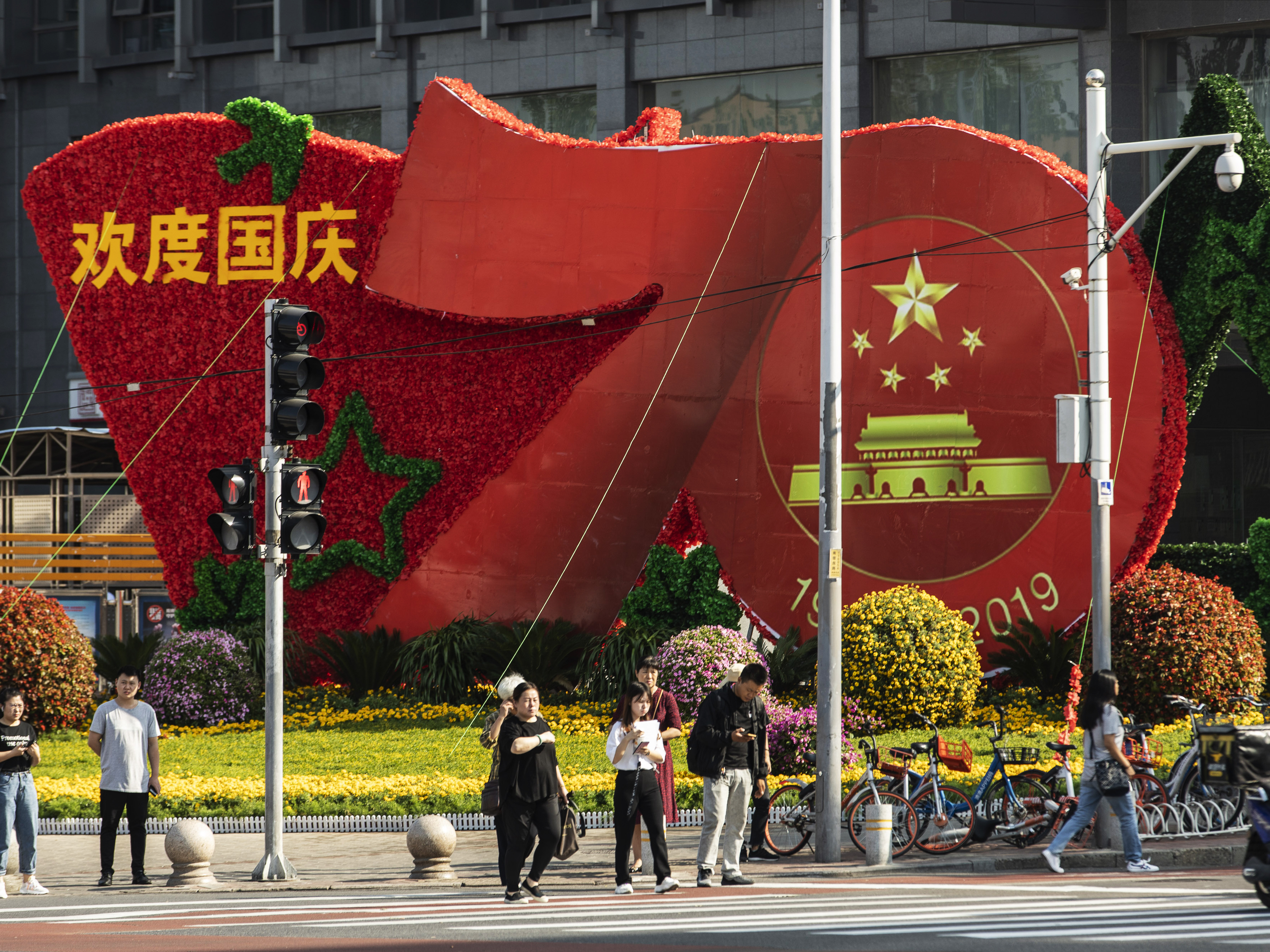 Pedestrians wait to cross a road in front of a floral installation celebrating the 70th anniversary of the Peoples Republic of China in Beijing. Streets have been cleaned and security increased before the Oct. 1 holiday.