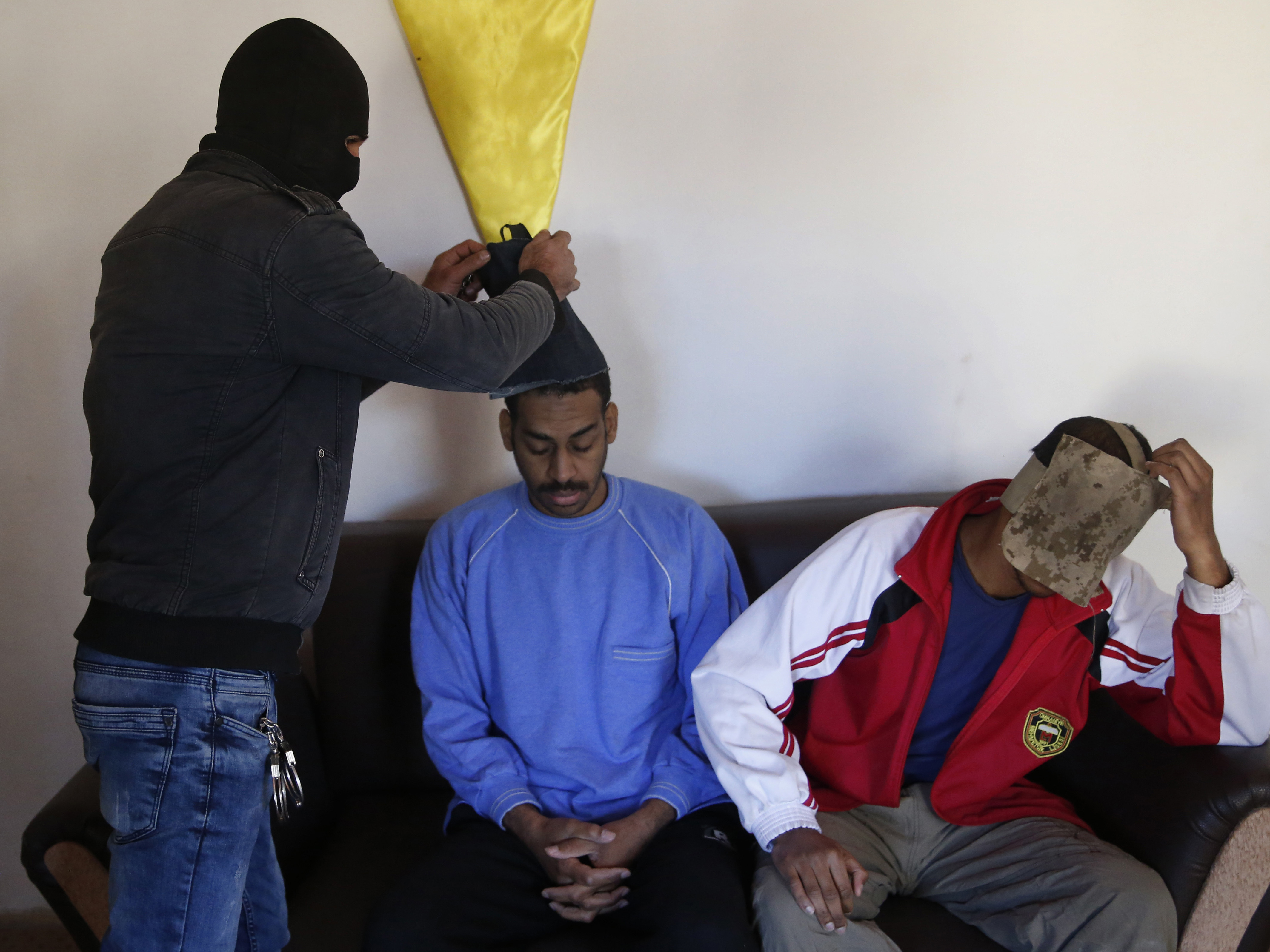 A Kurdish security officer takes off face masks from Alexanda Amon Kotey, left, and El Shafee Elsheikh, who were allegedly among four British jihadis who made up a brutal Islamic State cell dubbed "The Beatles," for an interview at a security center in Kobani, Syria, last year.
