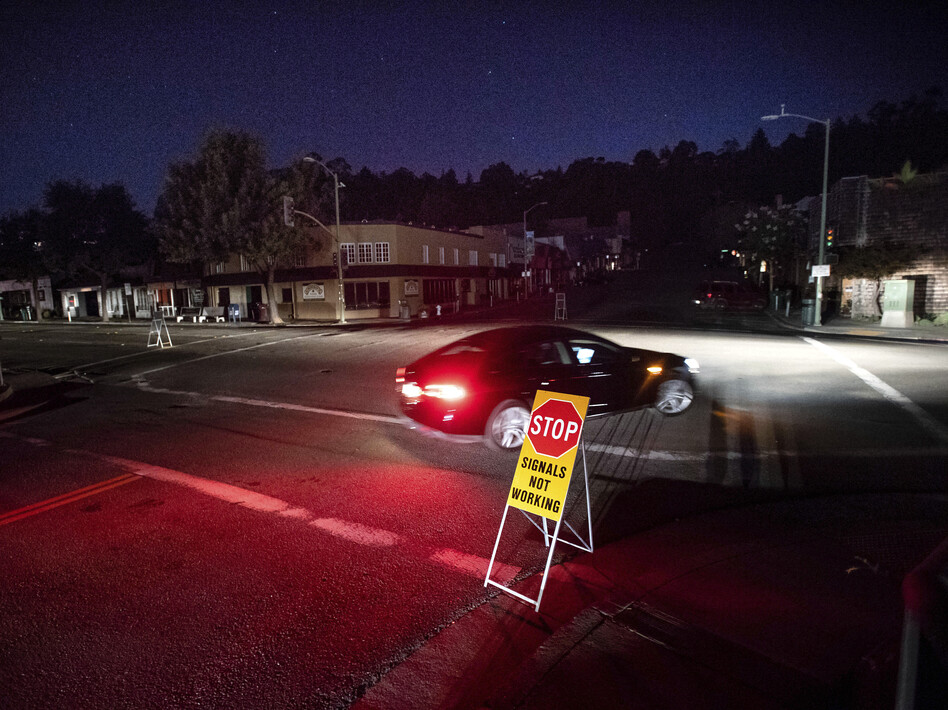 A car drives through a darkened Montclair Village during the power shutdown in Oakland, Calif., triggered by dry, windy weather. (Noah Berger/AP)