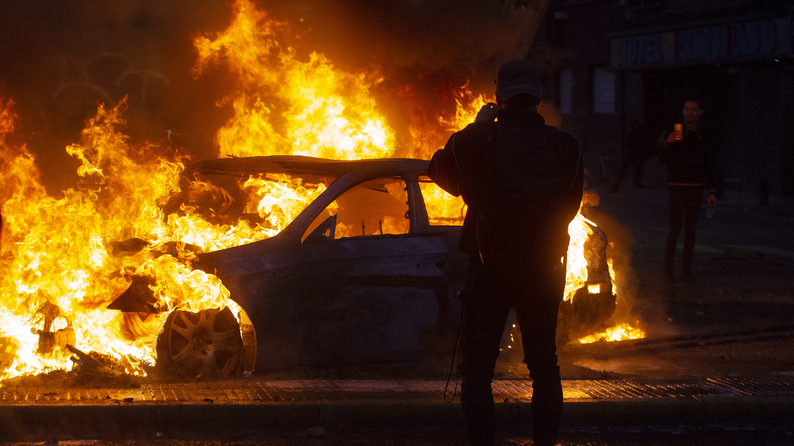 Men take pictures of a burning car during violent protests in Santiago Saturday. (AFP via Getty Images)
