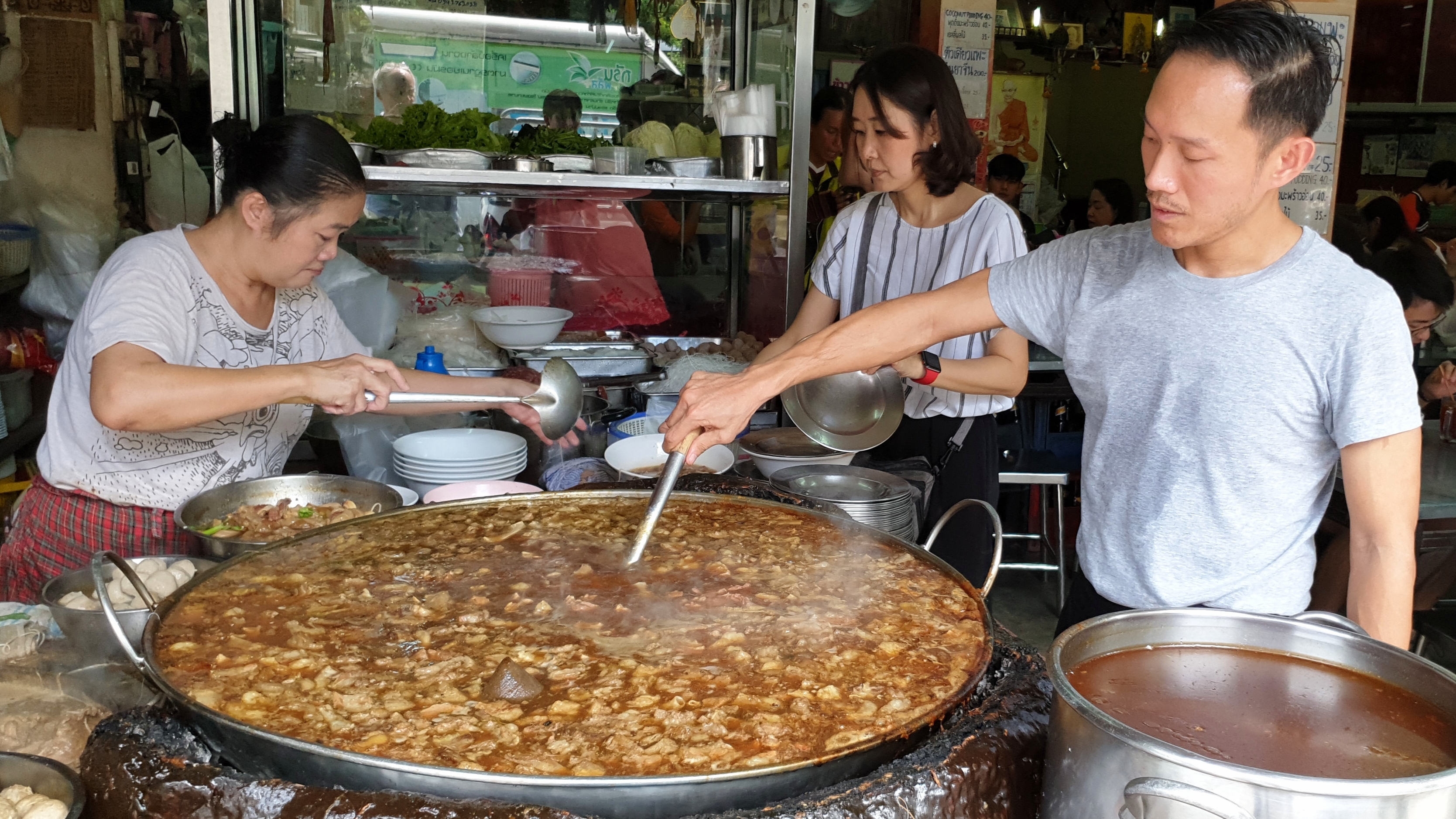 Nattapong Kaweeantawong, a third-generation owner of Wattana Panich, stirs the soup while his mother (left) helps serve and his wife (center) does other jobs at the restaurant. Nattapong or another family member must constantly stir the thick brew.