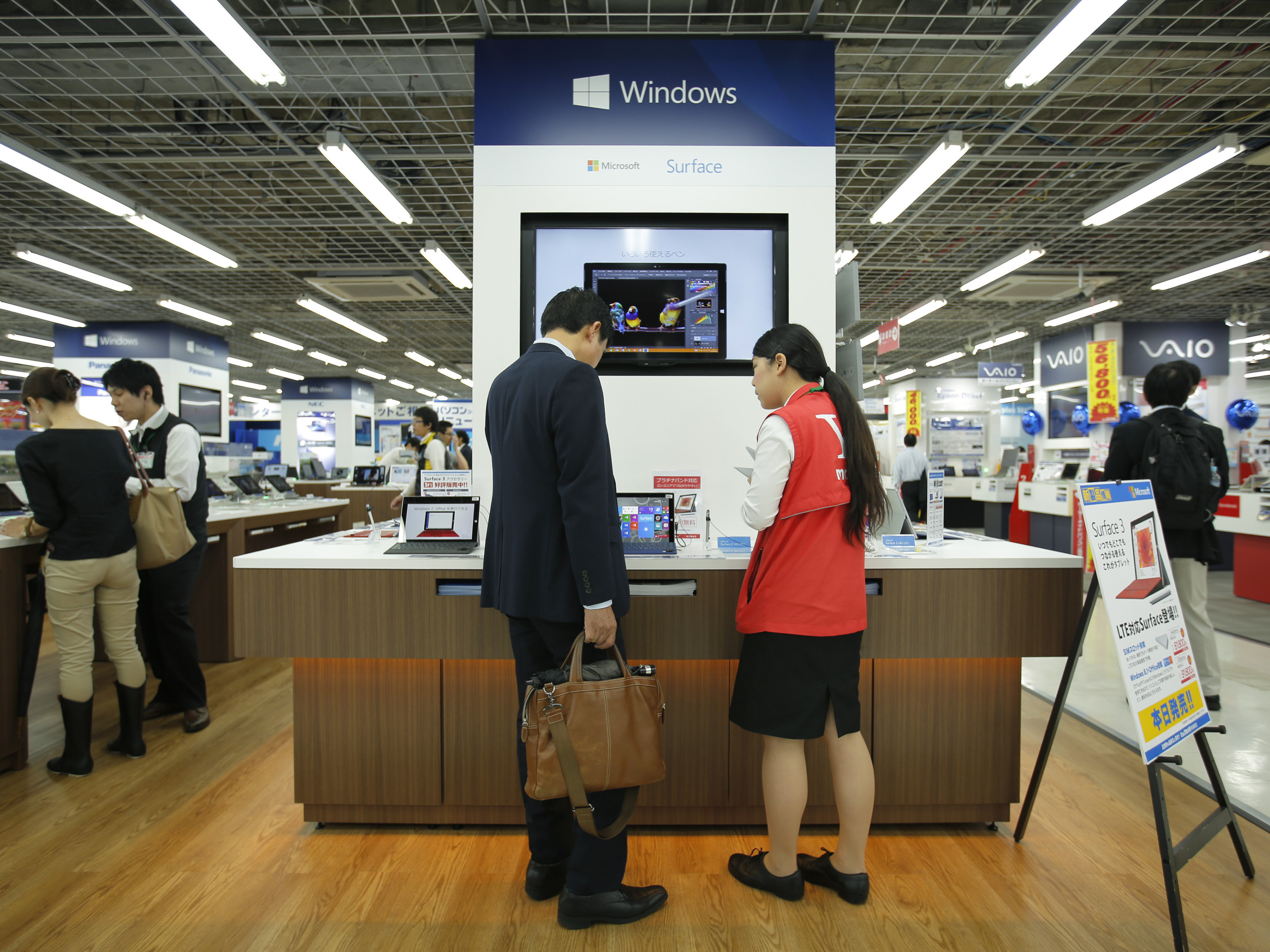 A sales clerk speaks with a customer in front of Microsoft Corp.'s display at an electronics store in Tokyo. Microsoft's division in Japan says it saw productivity grow by 40% after allowing employees to work for four days a week rather than five.