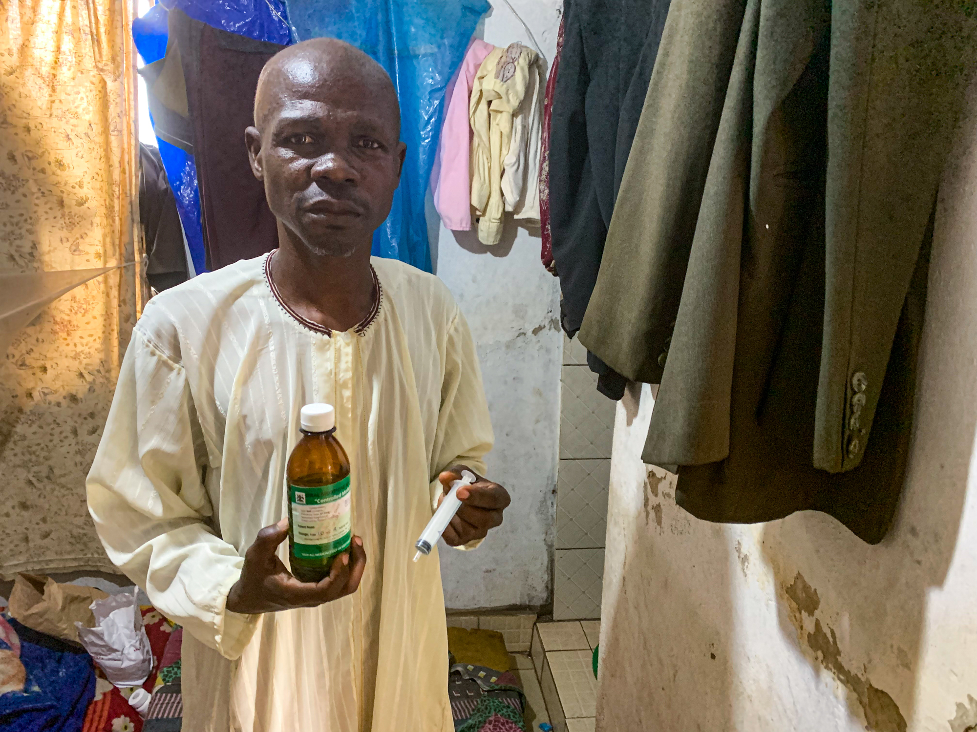 Ronald Mutyaba, an auto mechanic, at his home in Kampala, Uganda. Mutyaba is HIV positive and has developed Karposi sarcoma, a type of cancer that often affects people with immune deficiencies. He is holding a bottle of the liquid morphine that nurses from the nonprofit group Hospice Africa have prescribed to help control the pain caused by his illlness. (NPR)
