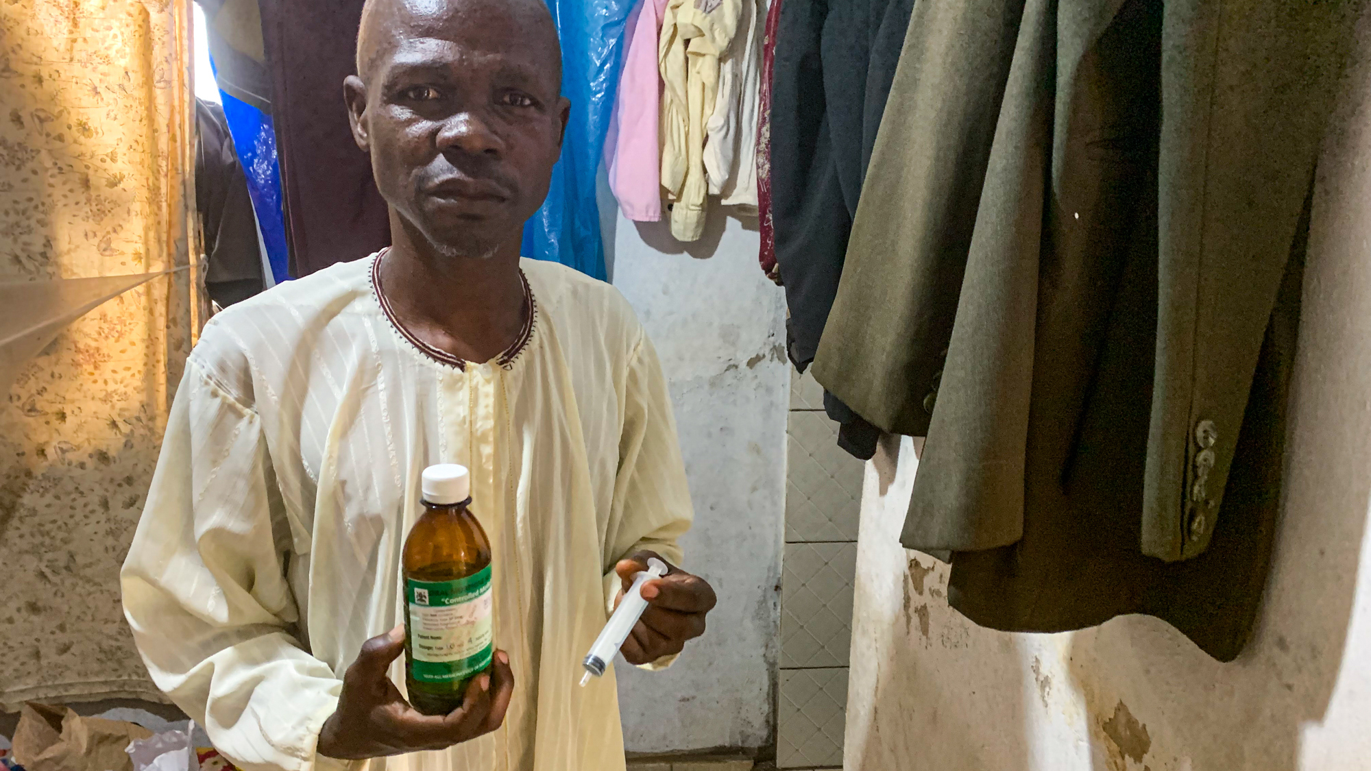 Ronald Mutyaba, an auto mechanic, at his home in Kampala, Uganda. Mutyaba is HIV positive and has developed Karposi sarcoma, a type of cancer that often affects people with immune deficiencies. He is holding a bottle of the liquid morphine that nurses from the nonprofit group Hospice Africa have prescribed to help control the pain caused by his illlness.