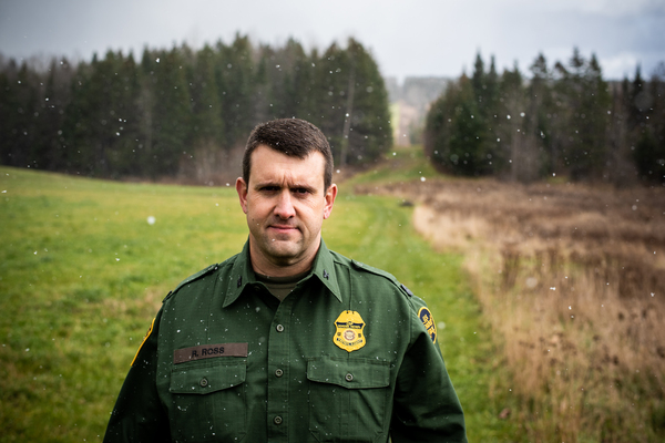 Richard Ross, patrol agent in charge of the United States Border Patrol's Newport Station, stands near the international boundary, marked by the slash in the forest, as snow falls.