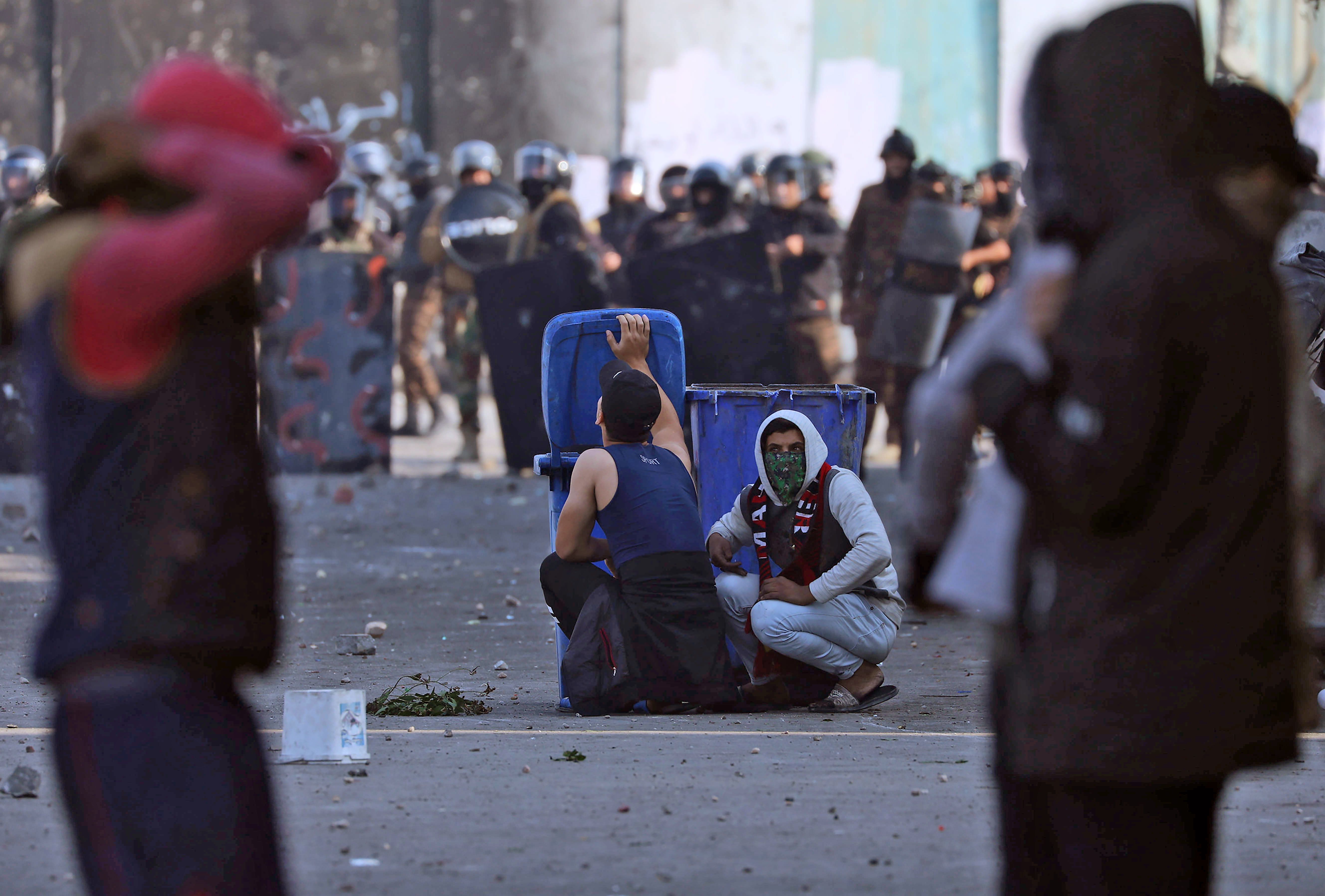 Iraqi demonstrators take cover from security forces behind trash cans during clashes in the city of Karbala on Thursday.