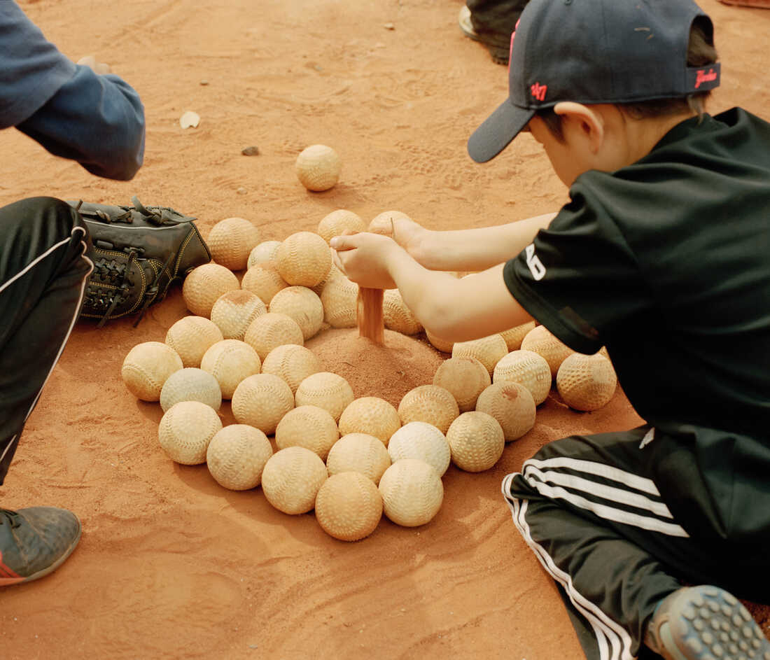 Children play in the sand of a baseball field next to a pile of baseballs.