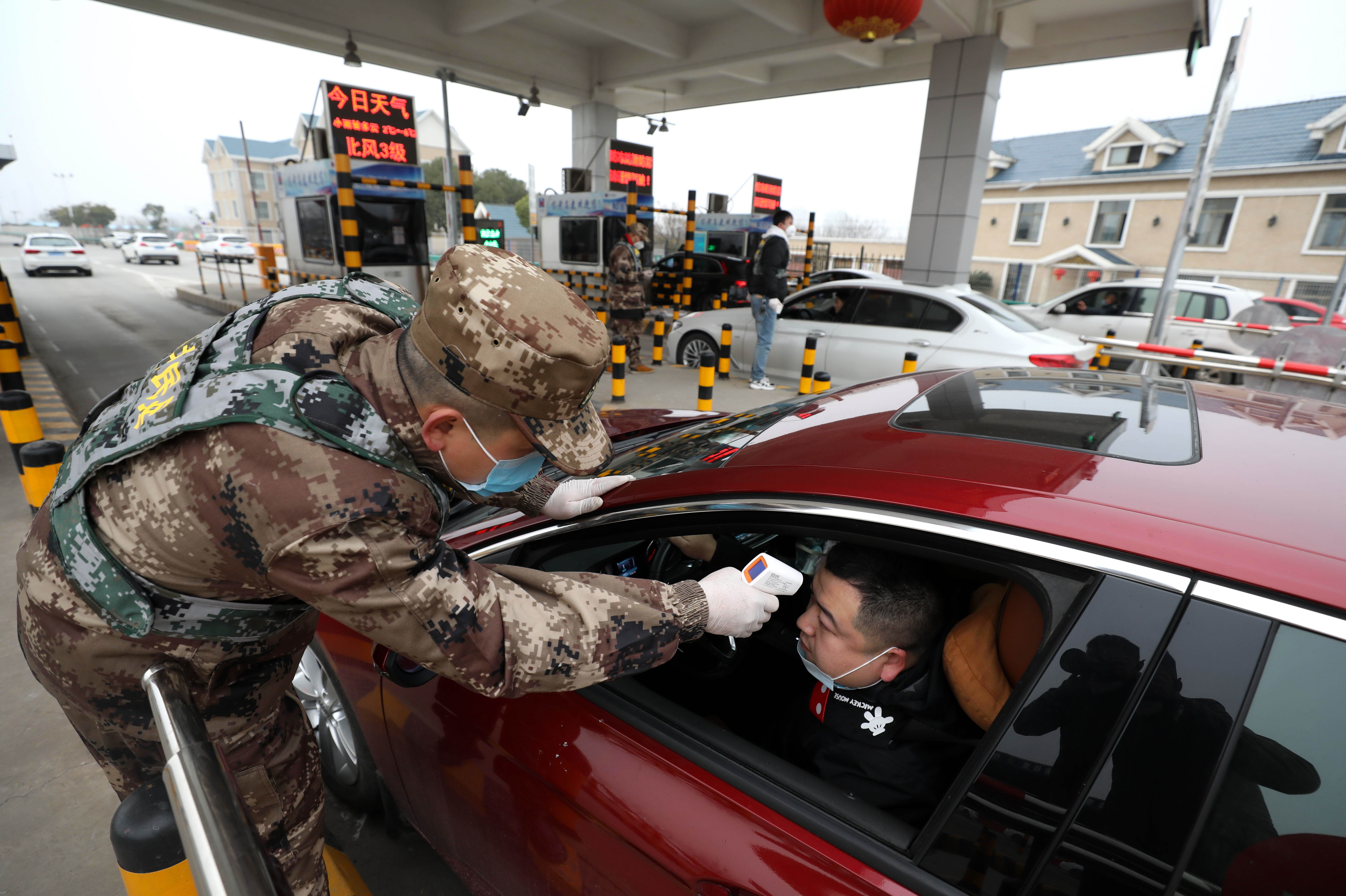 A militia member checks the body temperature of a driver at an expressway toll gate in Wuhan, China.