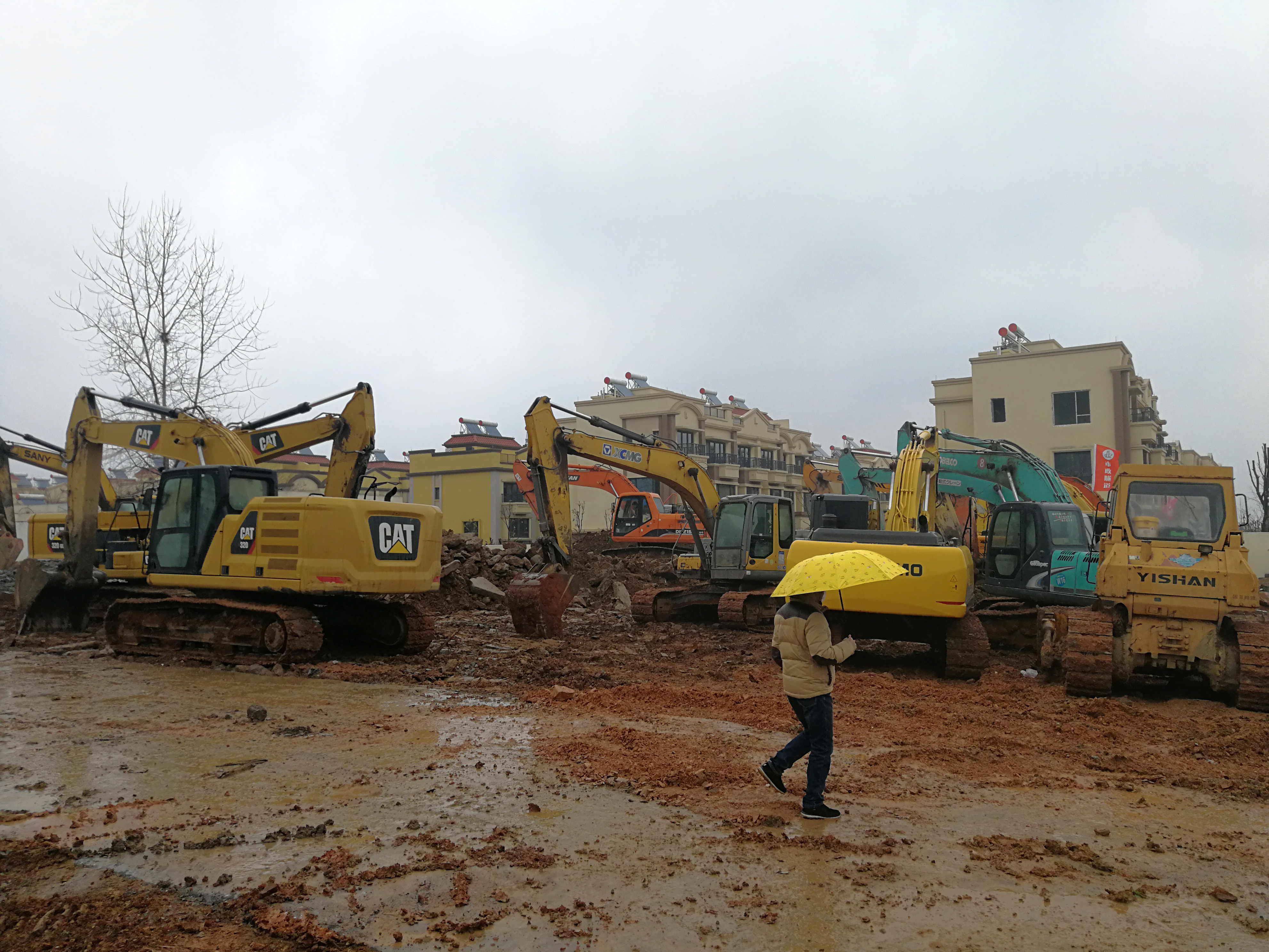 A man holding an umbrella walks past excavators at the construction site where a new quarantine and treatment center is being built to treat patients of a new coronavirus. (Reuters)