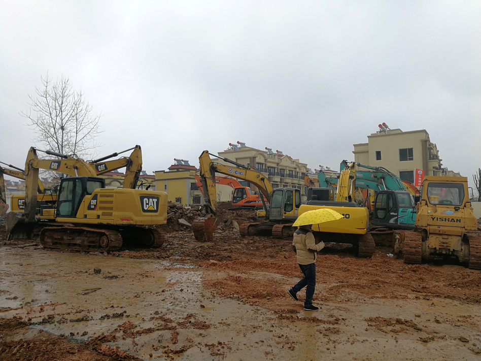 A man holding an umbrella walks past excavators at the construction site where a new quarantine and treatment center is being built to treat patients of a new coronavirus. (Reuters)