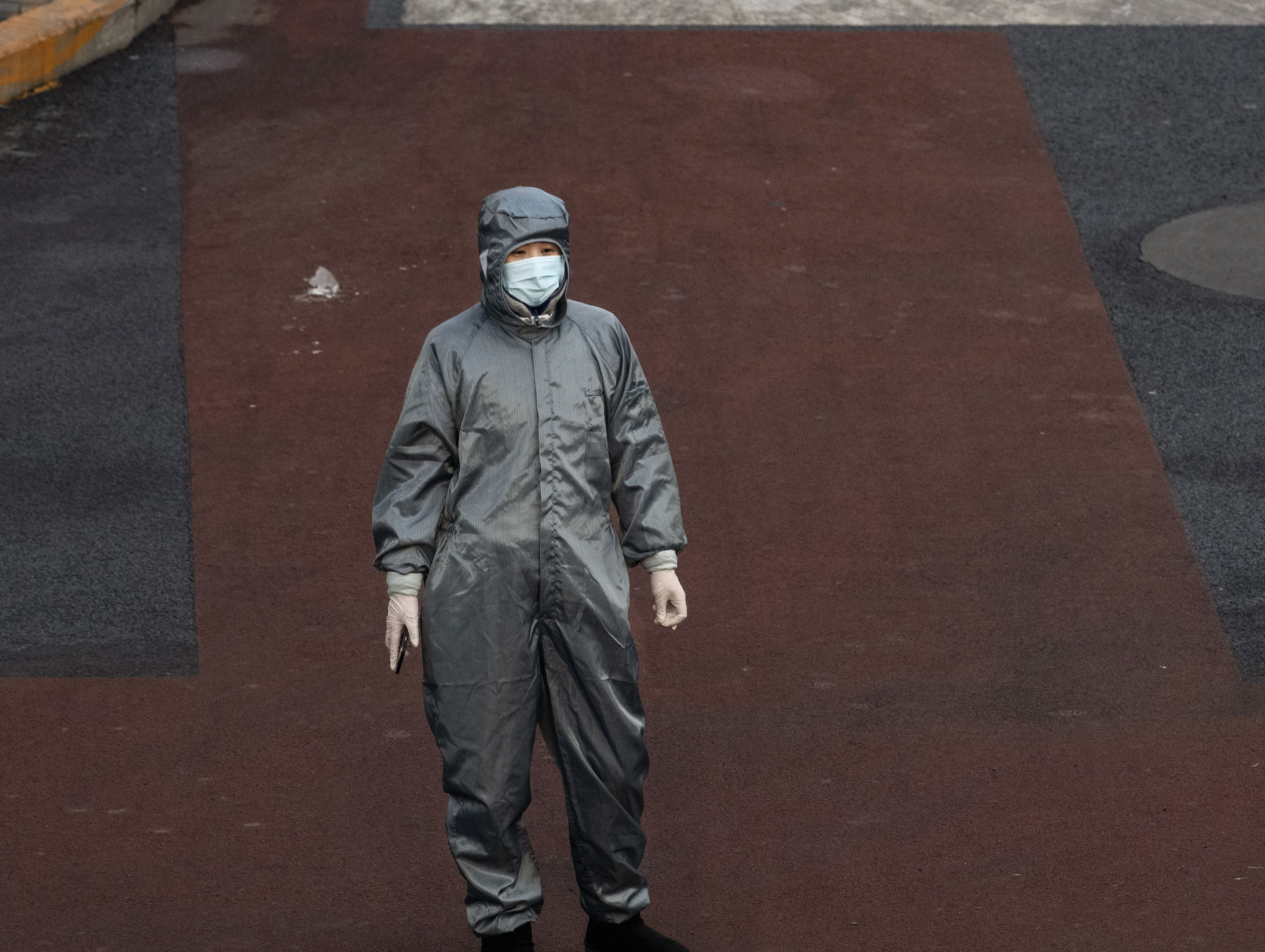 A Chinese woman wears a protective suit and mask as she waits to cross the intersection of a nearly empty Beijing on Saturday. (Getty Images)