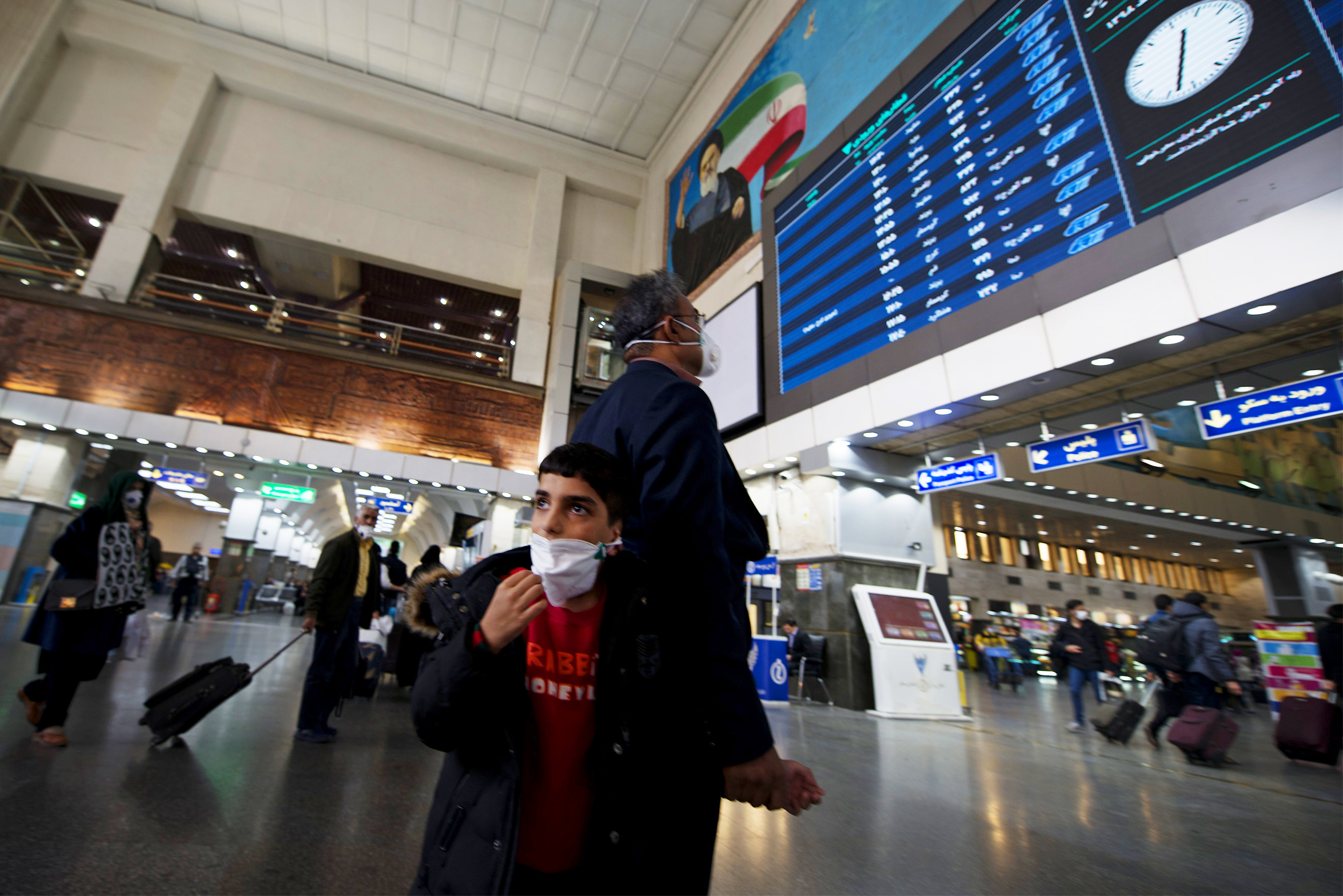 A father holding his son's hand while checking the information board in a train station in Iran's capital, Tehran. Schools were closed and many public gatherings, including Friday prayers, were canceled as the coronavirus spread in Iran, even infecting senior officials. (Marjan Yazdi for NPR)