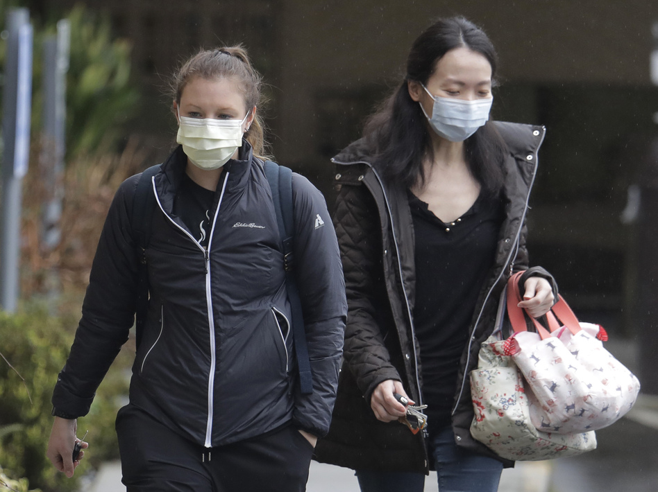Two women wearing masks walk away from the Life Care Center in Kirkland, Wash., near Seattle. An outbreak of the coronavirus is cited as the cause for the deaths of at least two residents at the center. (Ted S. Warren/AP)
