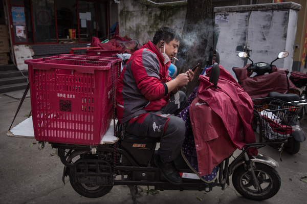 A worker with an empty cart on his scooter checks his phone.