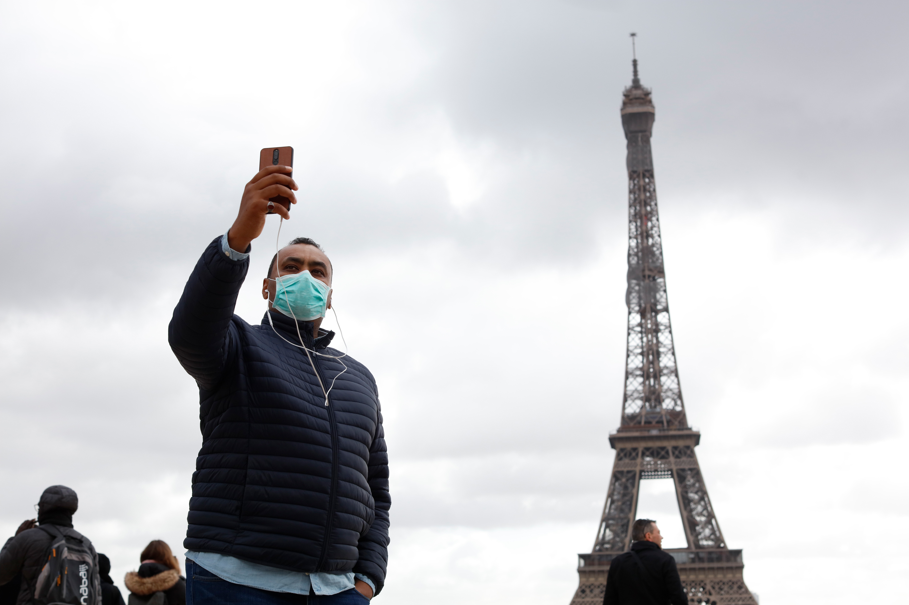 People with protective masks walk in front of the Eiffel Tower in Paris on March 9. The new coronavirus has had an impact on international travel. (NurPhoto via Getty Images)