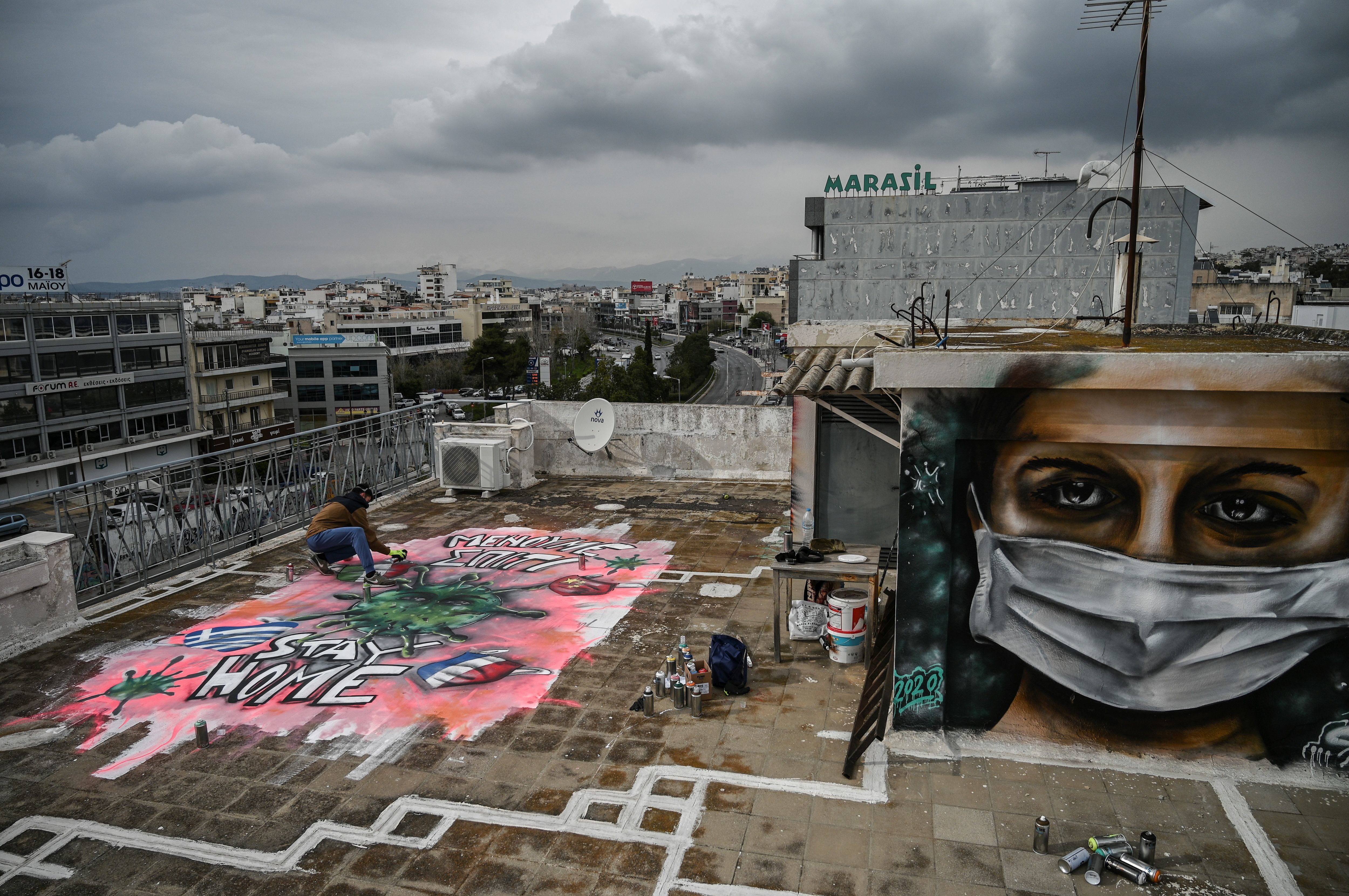 Street artist S.F. paints a mural about the COVID-19 crisis on the roof of his building in Athens, Greece, on Monday. (AFP via Getty Images)