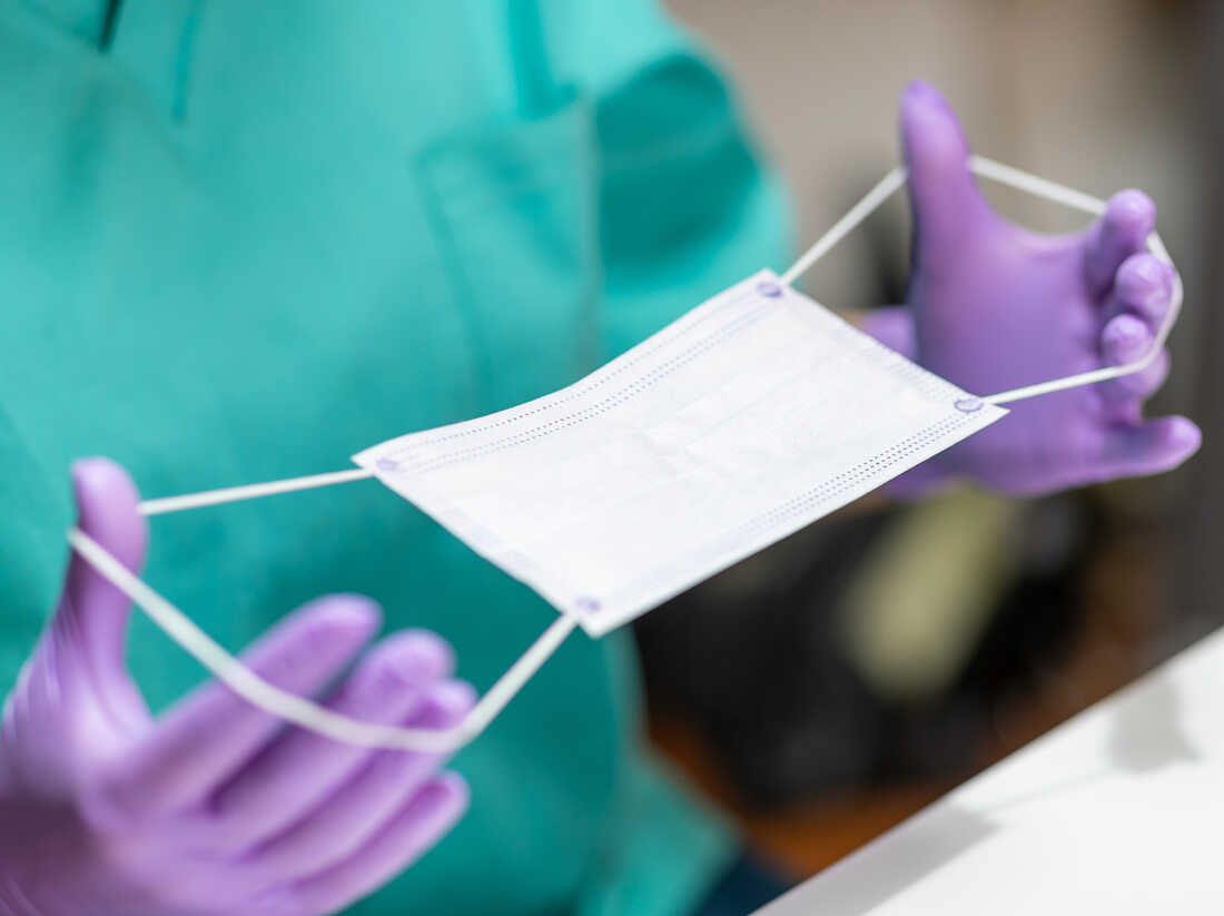 Hands in protective gloves holding stretching bands on protective mask for application.