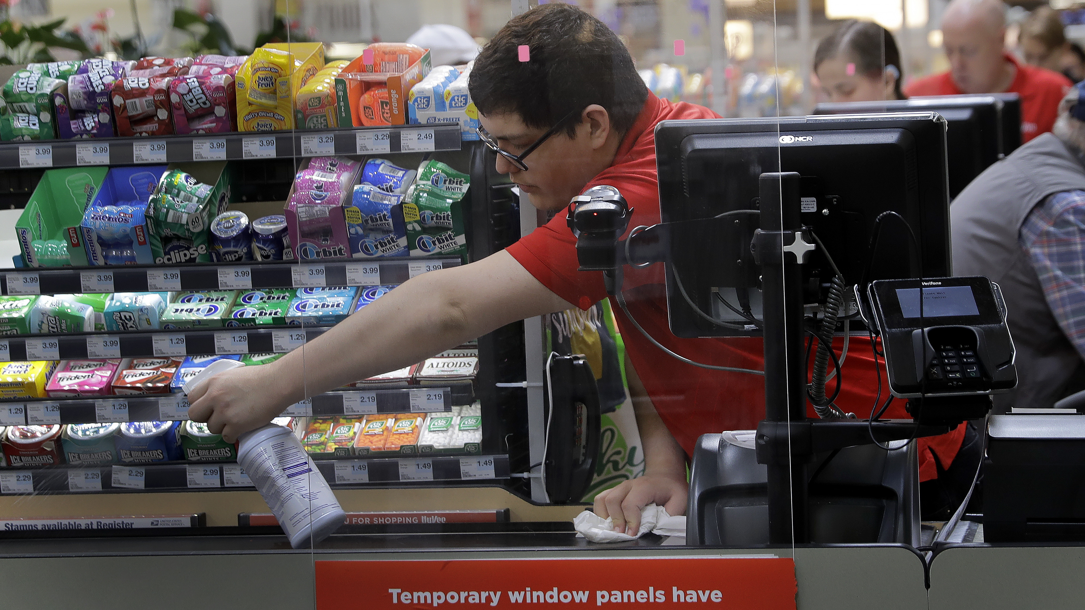 Garrett Ward sprays disinfectant behind a plexiglass panel at a Hy-Vee grocery store in Overland Park, Kan., on March 26. Stores have begun installing the shields in checkout aisles to protect clerks and help stop the spread of the coronavirus.