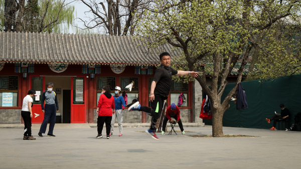 A skilled player of jianzi, or the Chinese equivalent of Hackey Sack, jumps to pass the feathered toy to the next participant.