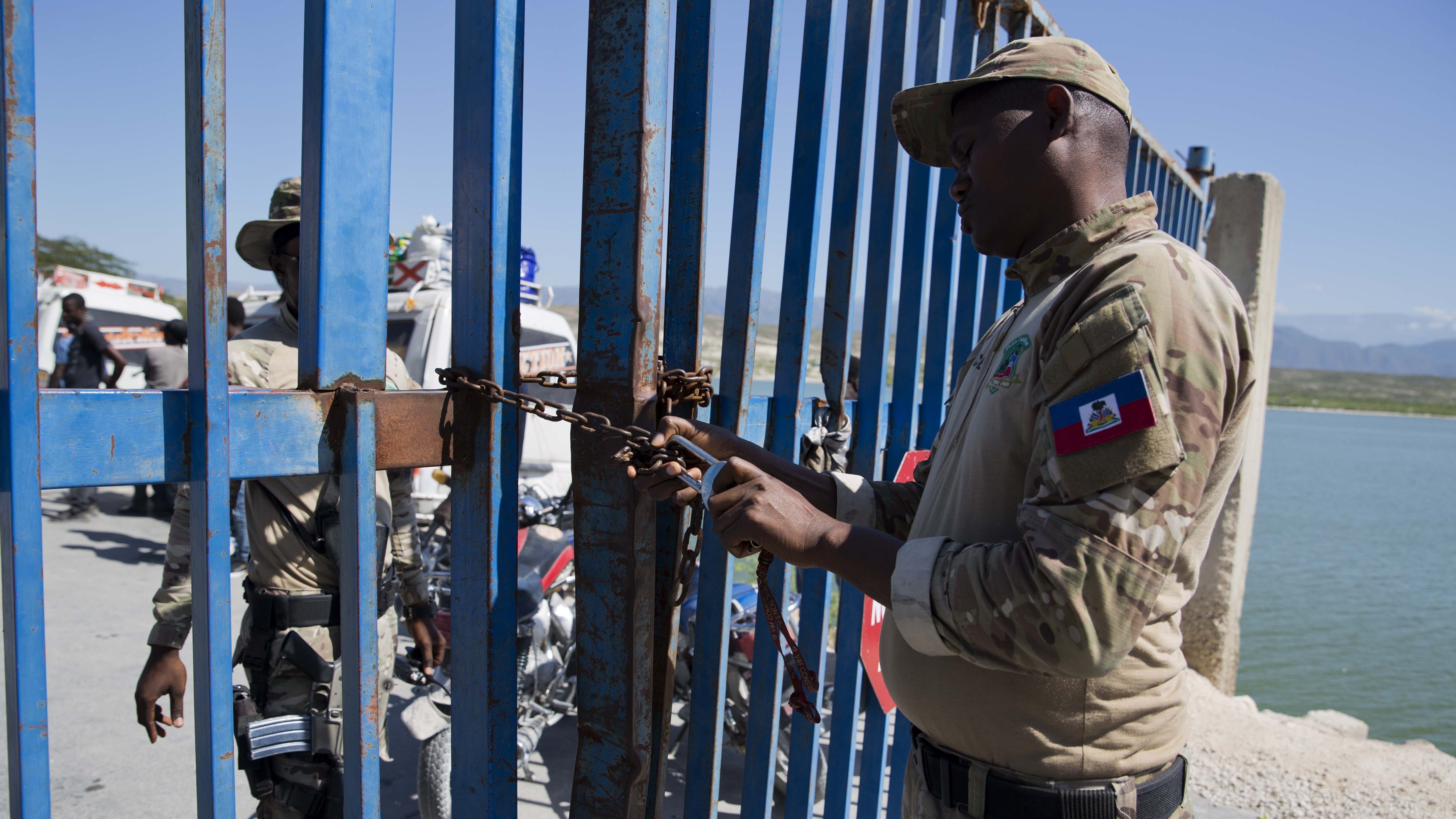 A Haitian police officer locks a gate that separates the Dominican Republic border town Jimani from Malpasse, Haiti, last month, as Haitian authorities shut down the border because of concerns over the spread of COVID-19.