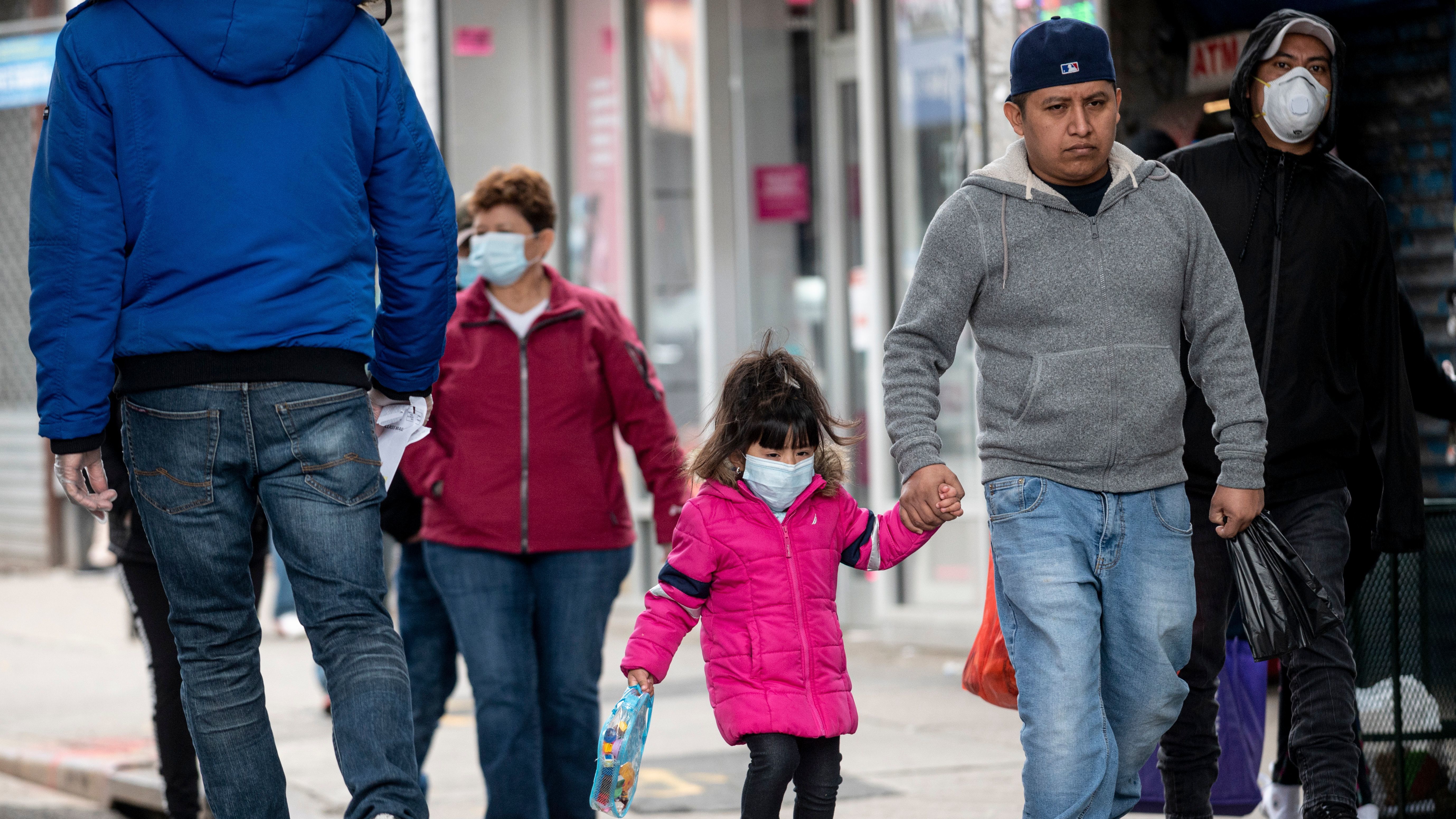 People, some wearing masks, walk down a street in the Corona neighborhood of Queens in New York on Tuesday. (AFP via Getty Images)