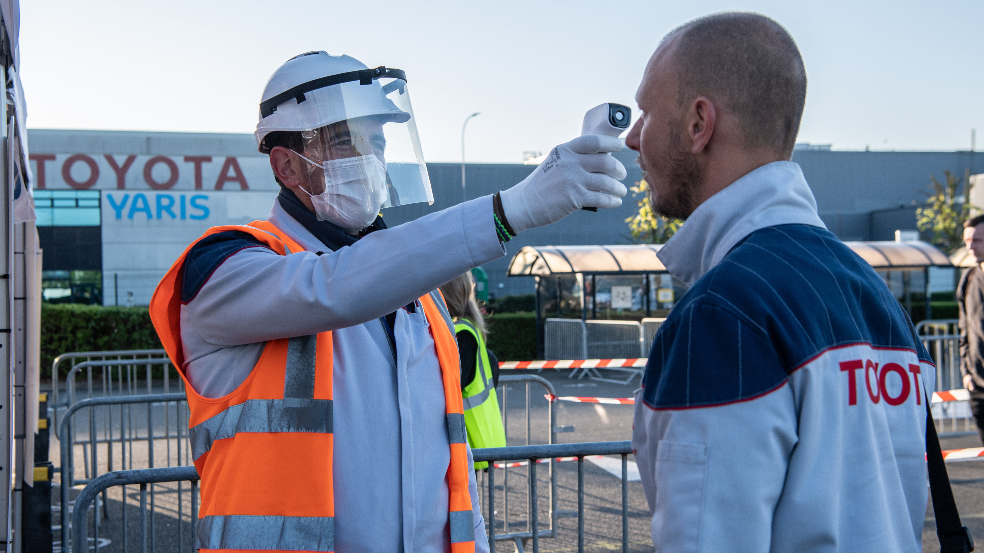 A worker wearing protective gear checks an automobile assembly line worker's temperature at the entrance to a Toyota plant in Onnaing, France, on April 21. U.S. auto plants are preparing to reopen with new coronavirus safety protocols. (Bloomberg via Getty Images)