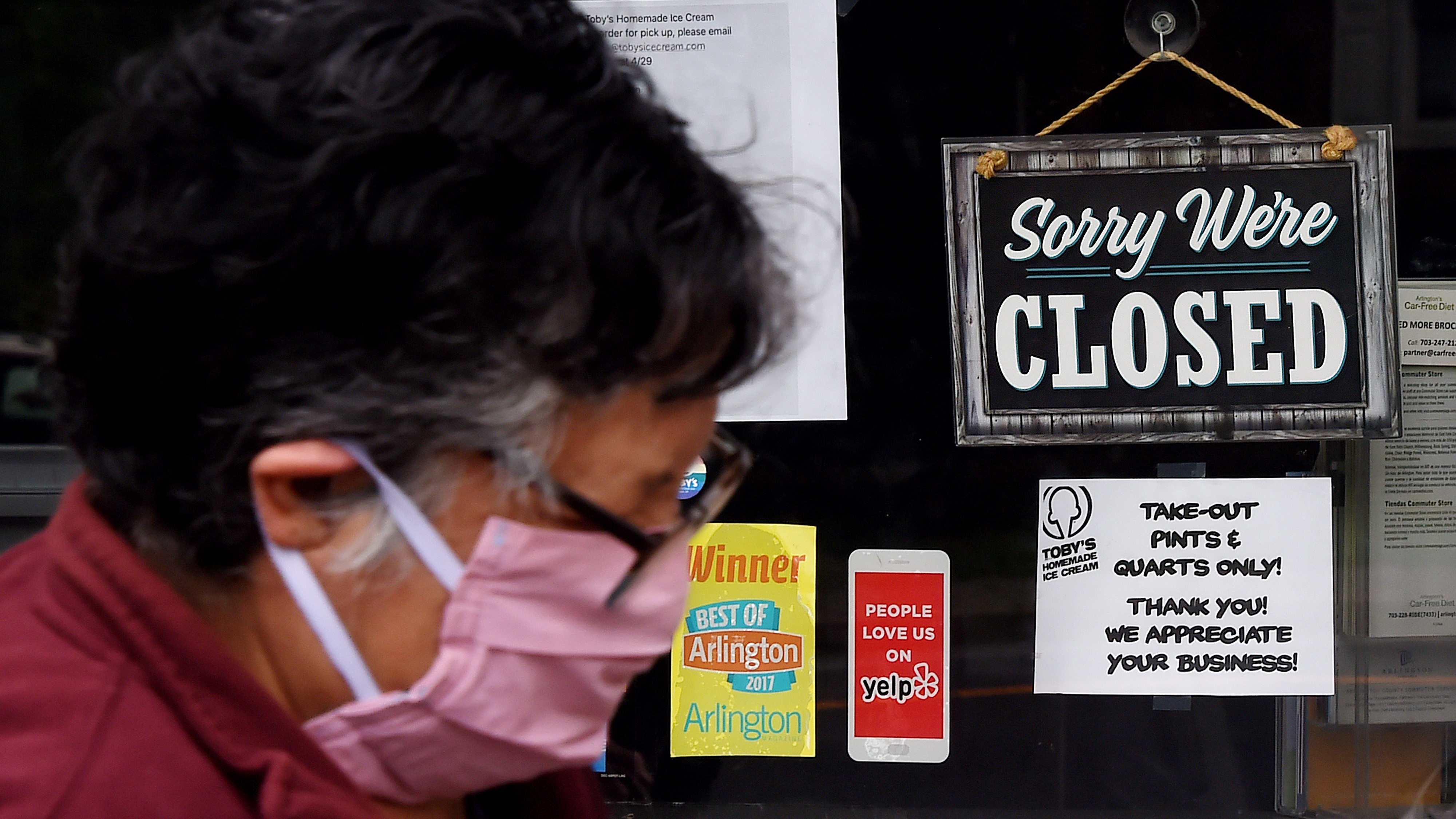 A woman wearing a face mask walks past a sign in the window of a food store in Arlington, Va., Tuesday. Business groups say members are worried about liability issues as they reopen. (AFP via Getty Images)