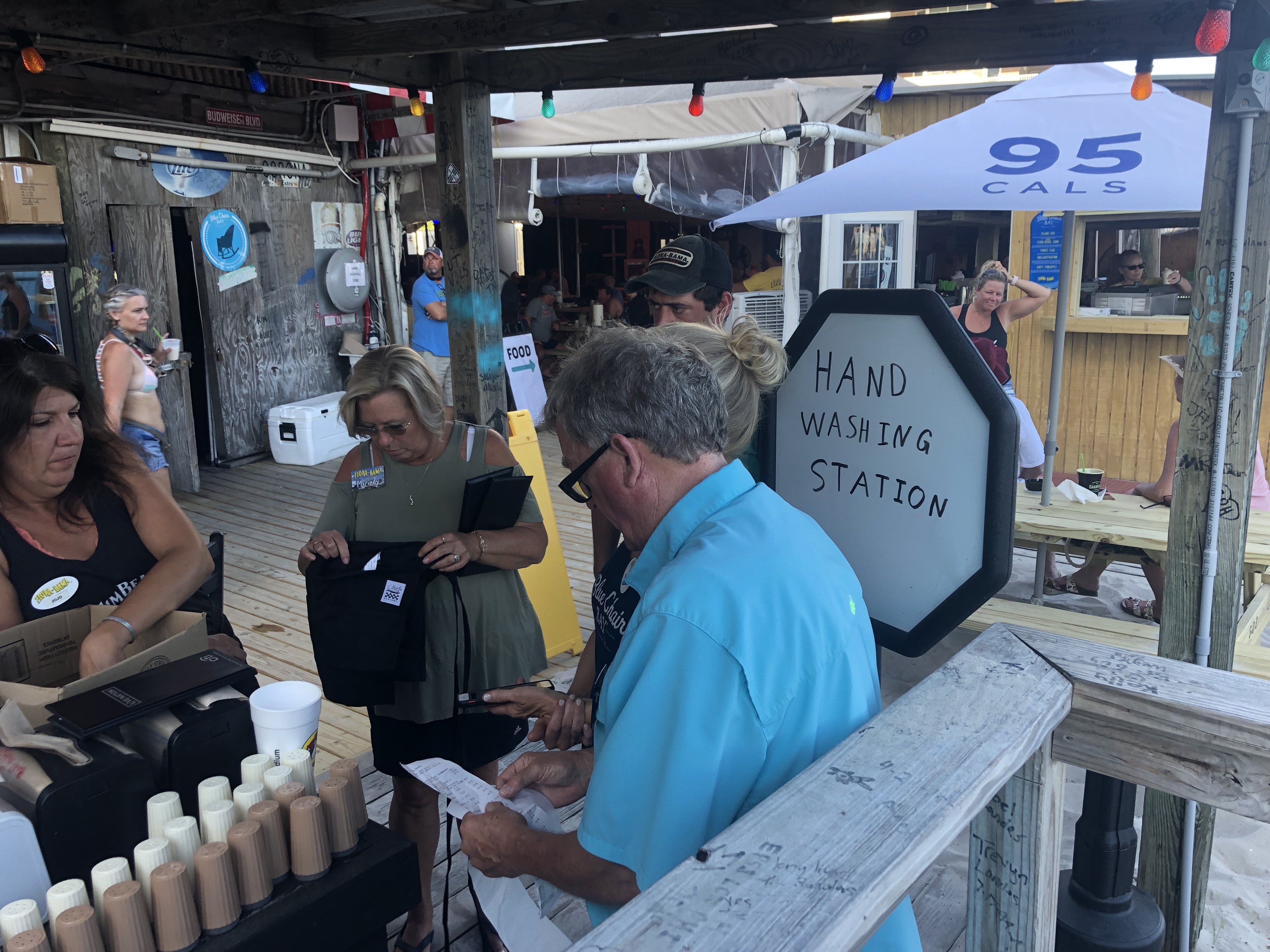 Servers go through a shift change at a makeshift hand-washing and sanitizer station outdoors at the Flora-Bama roadhouse in Perdido Key, Fla. Florida allowed restaurants to open this week at limited capacity and with new safety protocols. (NPR)