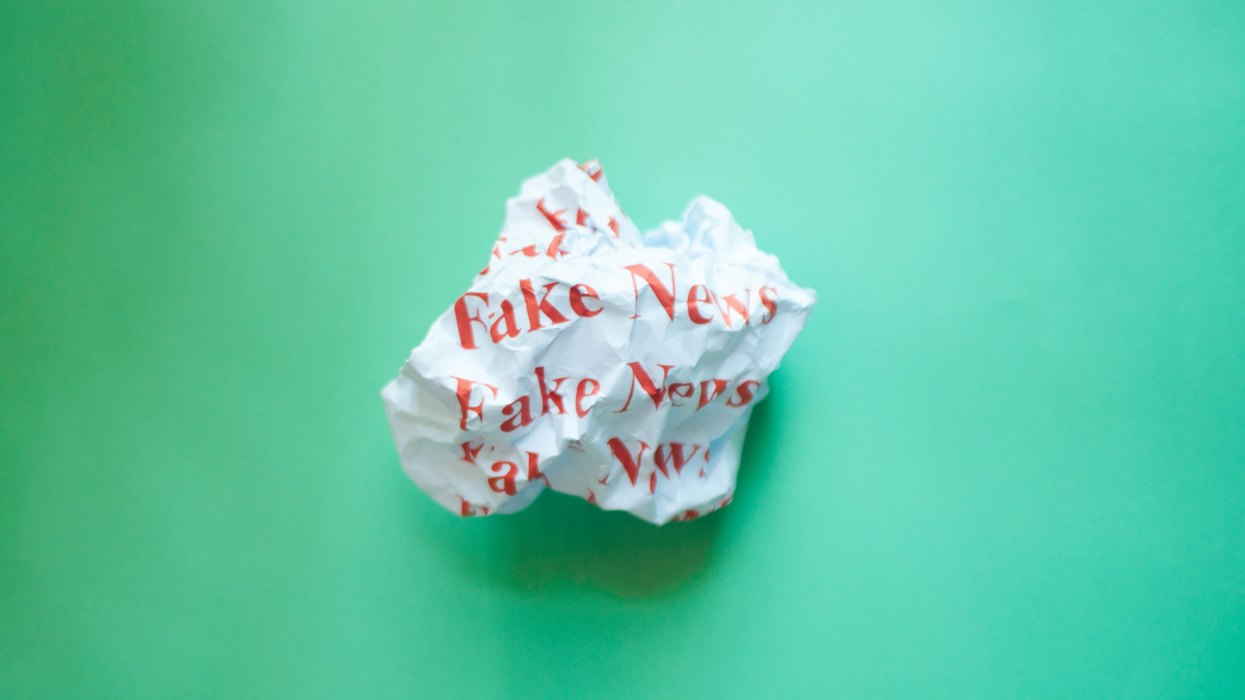 Crumpled paper with red font fake news against blue green background. (Getty Images)