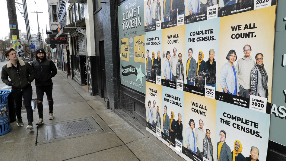 People walk past posters encouraging participation in the 2020 census in April in Seattle. A group of House Democrats have introduced a bill that would grant the U.S. Census Bureau's request to delay major deadlines for delivering results of the count because of the pandemic. (Ted S. Warren/AP)
