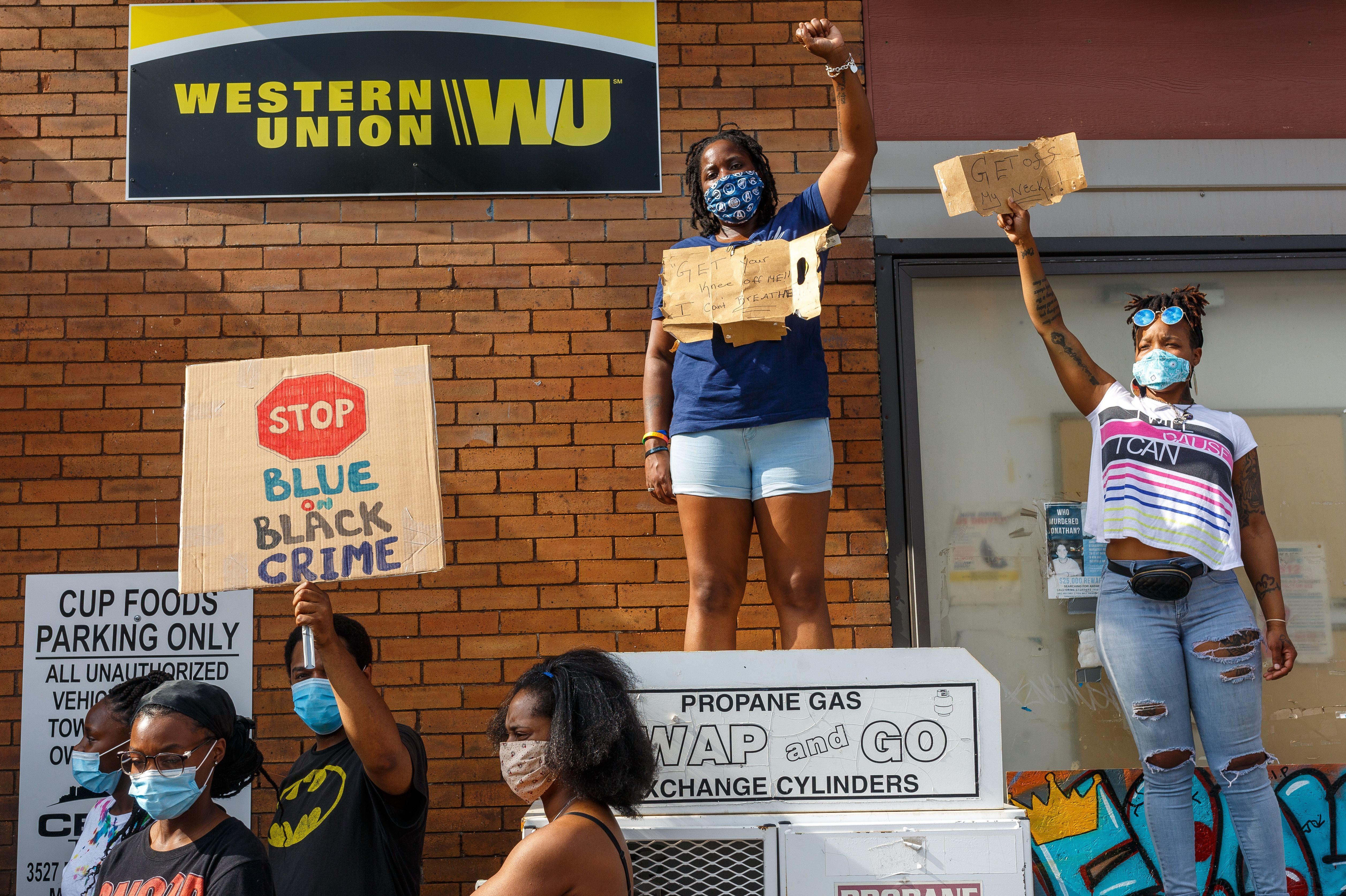 Women hold signs while protesting near the area where a Minneapolis Police Department officer allegedly killed George Floyd, on Tuesday in Minneapolis, Minn. A 10-minute <a href=&quot;https://www.facebook.com/darnellareallprettymarie/videos/1425398217661280/&quot;>video widely circulated on social media</a>  shows a police officer using his knee to pin the man's neck to the ground for multiple minutes. (AFP via Getty Images)