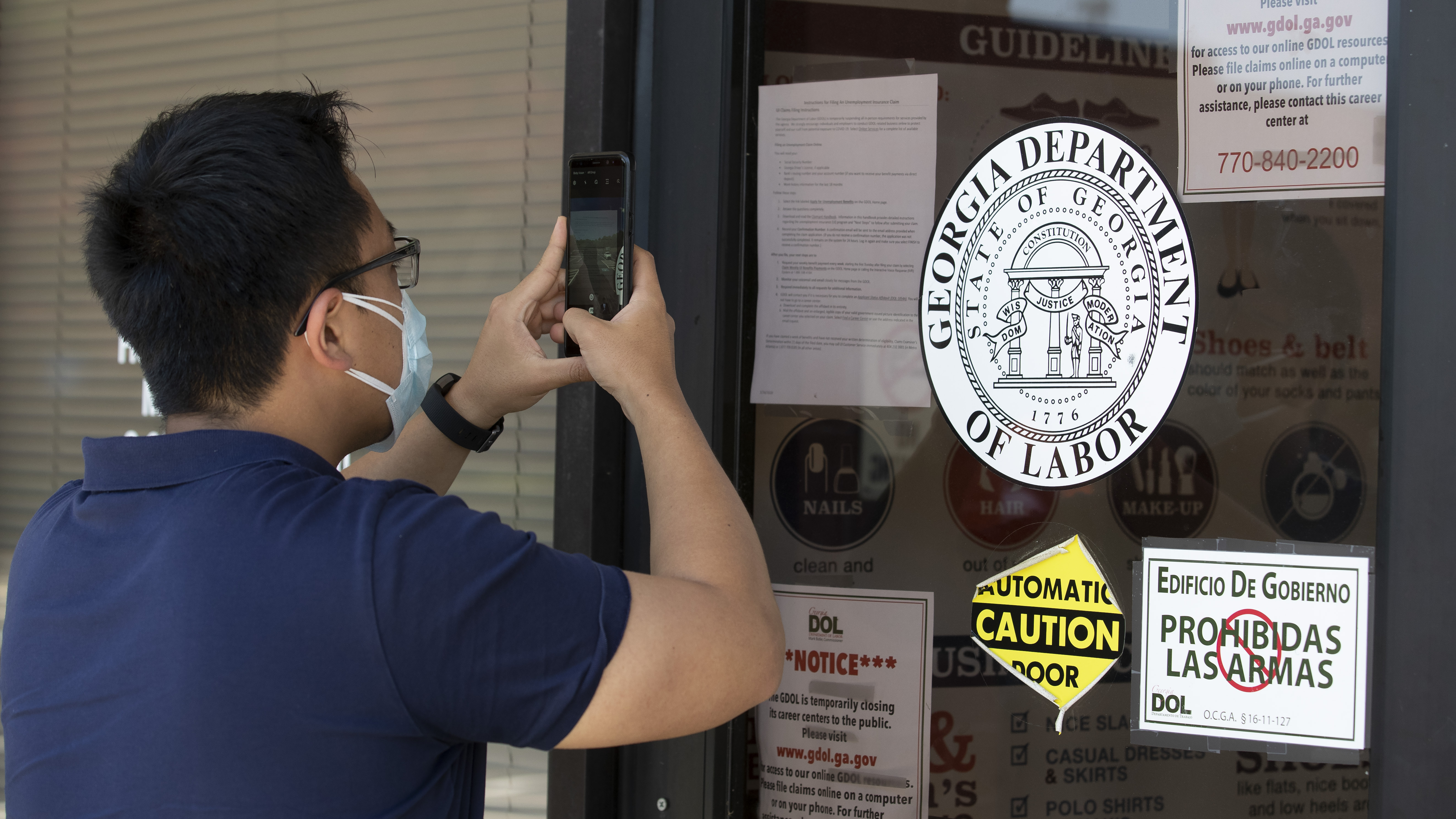 A man copies phone numbers posted on the locked doors of a Georgia Department of Labor office in in Norcross, Ga. Millennials are facing the second — or even third — economic downturn of their adult lives.