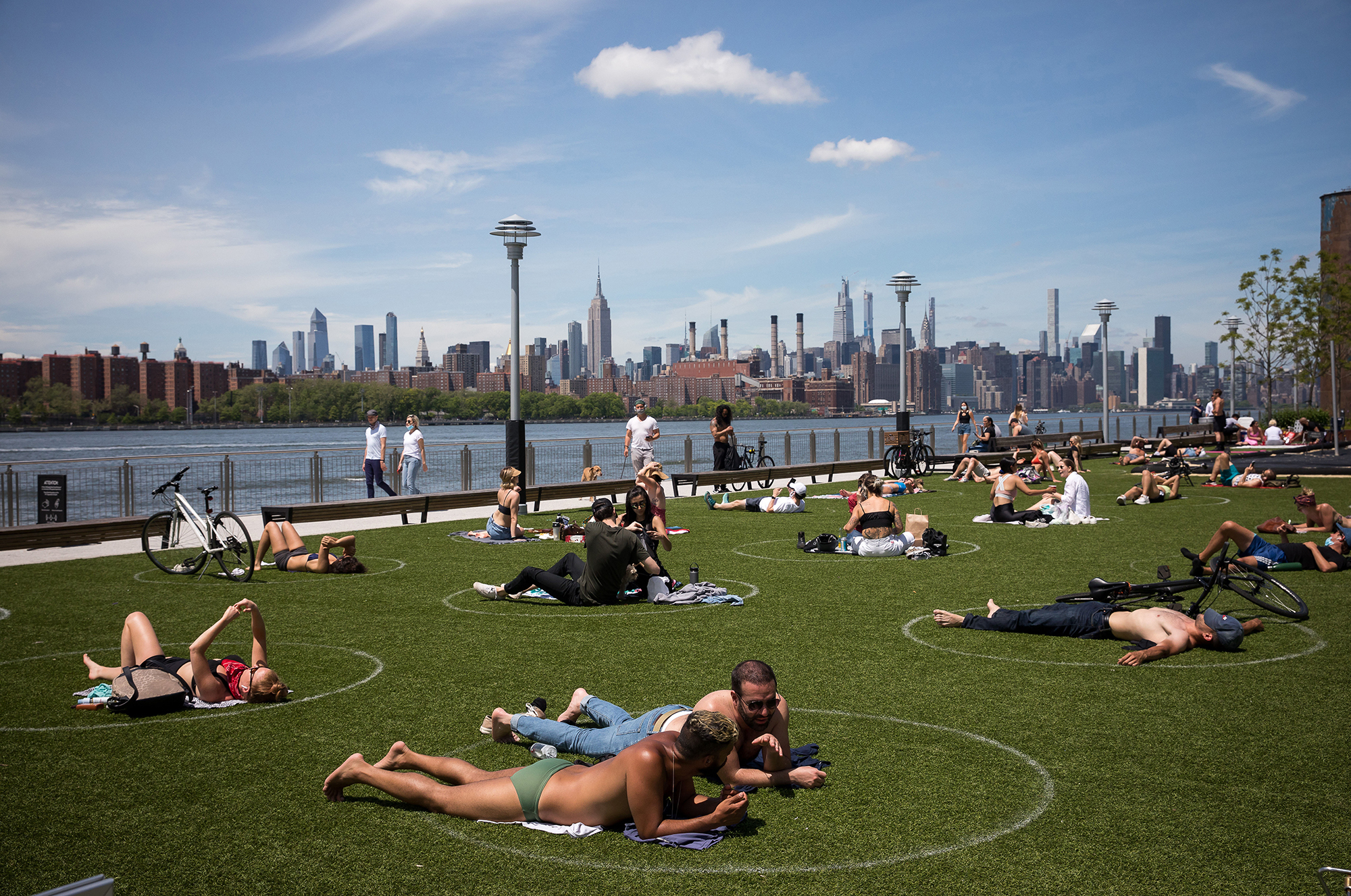 People rest inside social distancing markers at Domino Park in the Brooklyn borough of New York in late May. Stay-at-home orders in New York helped to lower the state's &quot;reproduction number,&quot; which estimates how many people one sick person could infect with the coronavirus. (Xinhua News Agency/Getty Images)