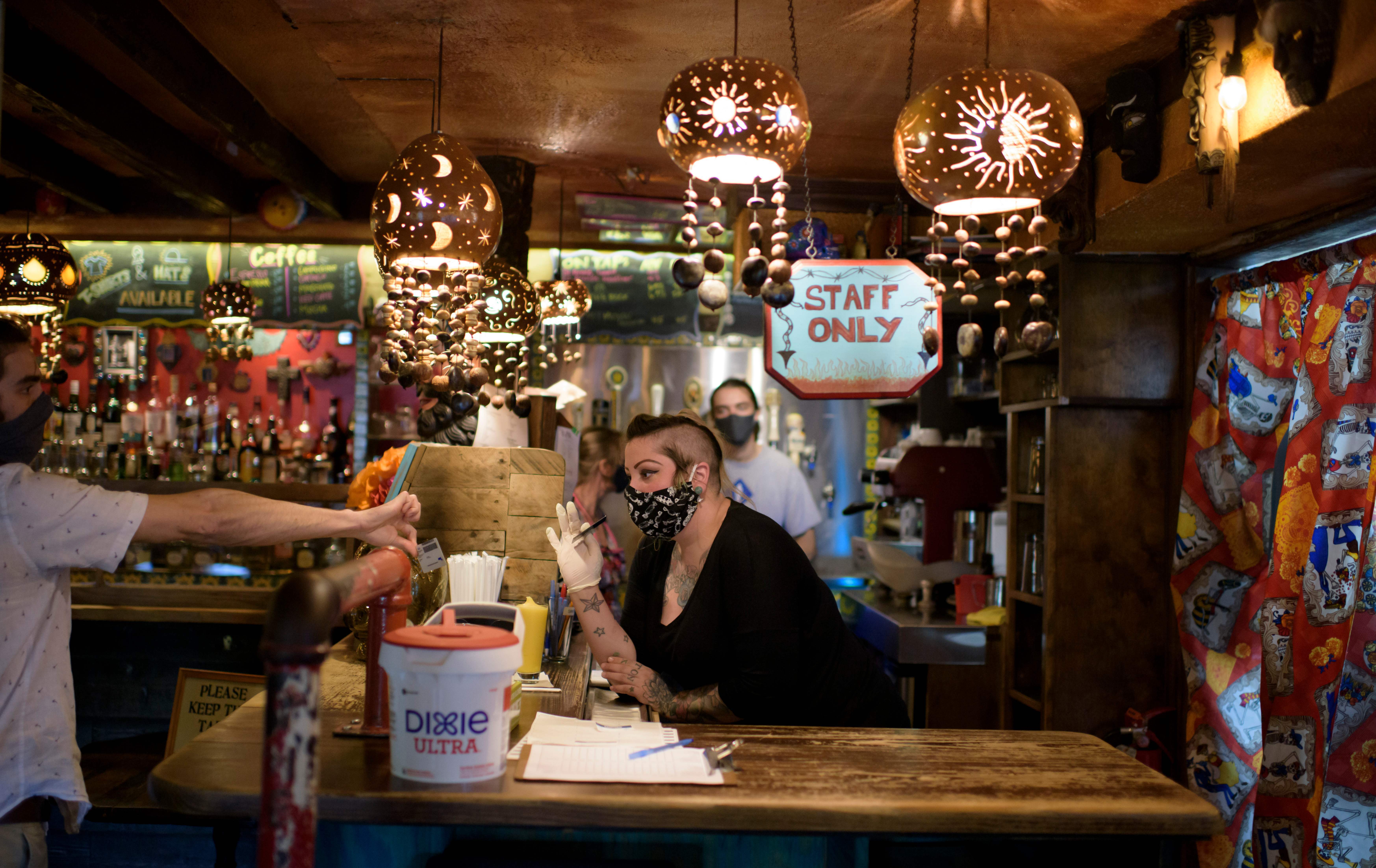 A bartender wearing a face mask and gloves checks a patron's ID at Under the Volcano in Houston last month. Texas is one of the states seeing a big uptick in coronavirus cases and hospitalizations. (AFP via Getty Images)